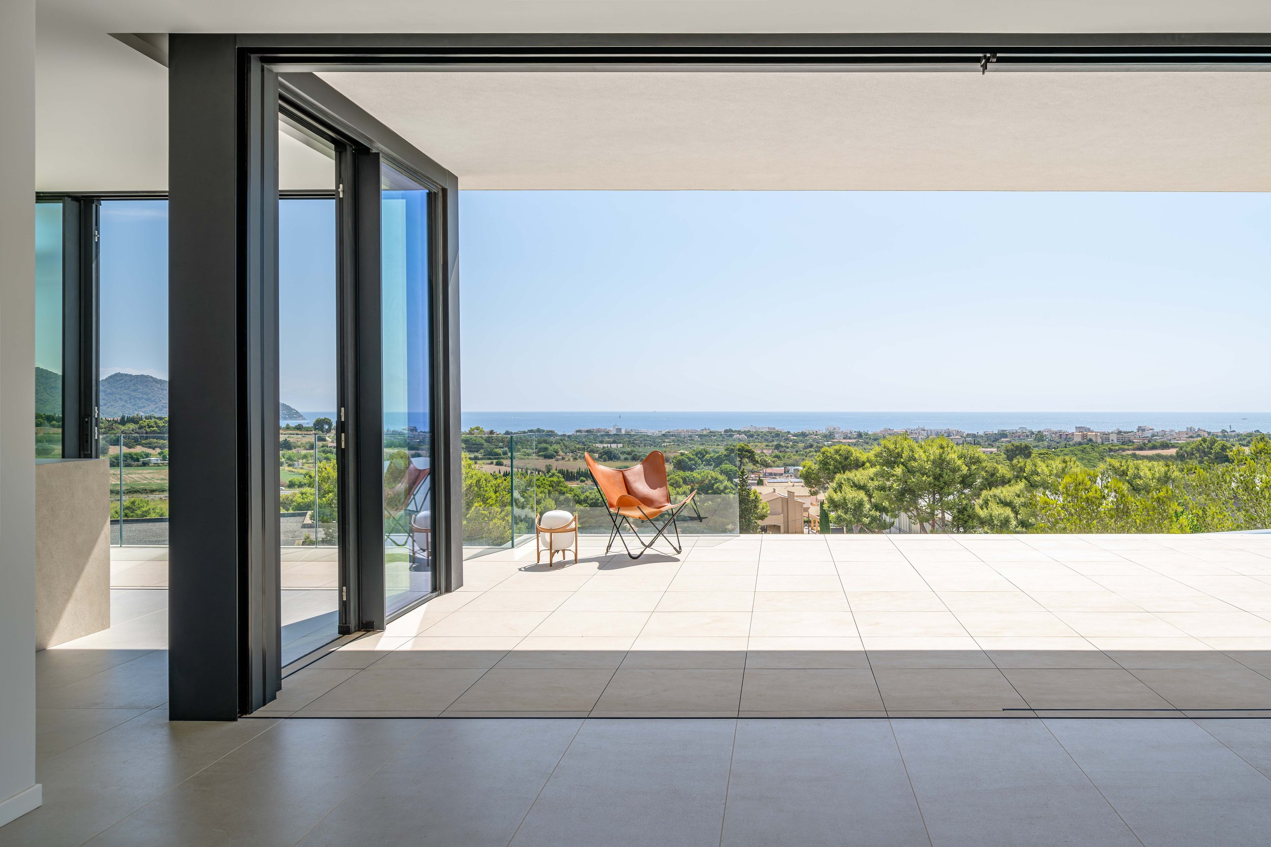 Terraza moderna con vista panorámica al mar y paisaje verde, con silla de cuero y mesa en el balcón