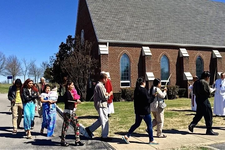A diverse group of people walking in a line outside All Saints' on a sunny day.