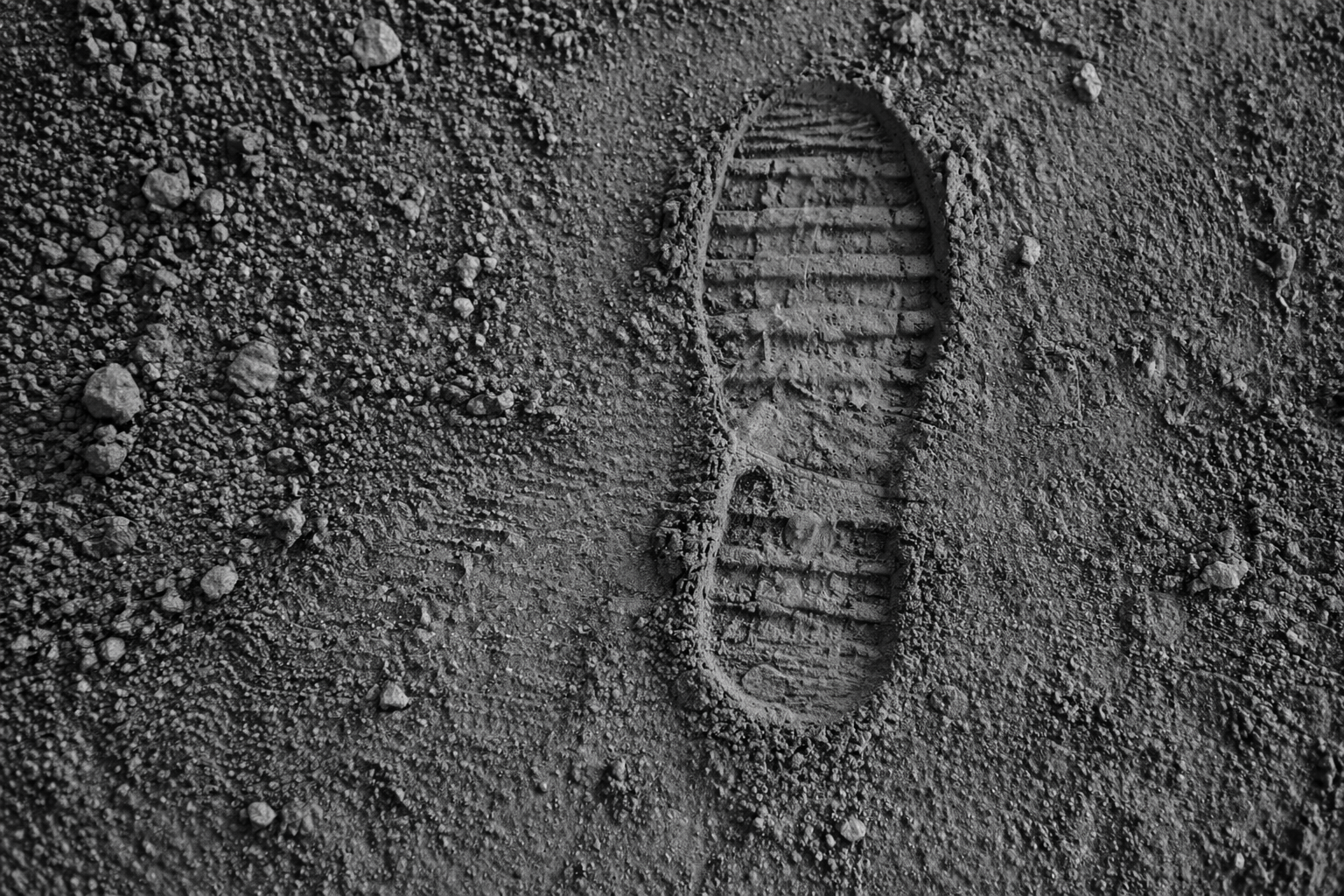 A single footprint in the dirt, surrounded by small rocks and gravel.