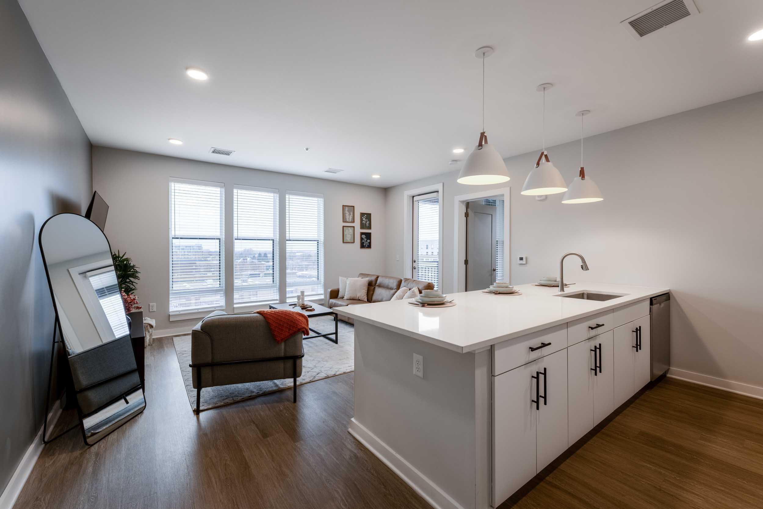Open-concept living room with large windows, a sectional sofa, and a kitchen island with pendant lights.