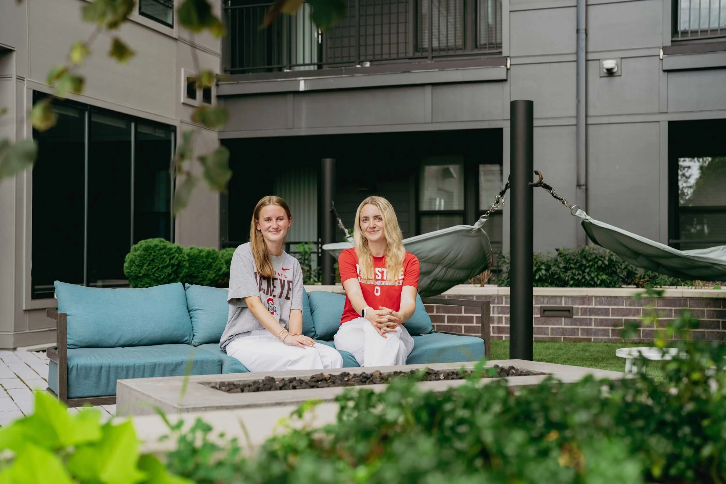 Two women sitting on a blue outdoor sofa in a modern apartment complex courtyard.