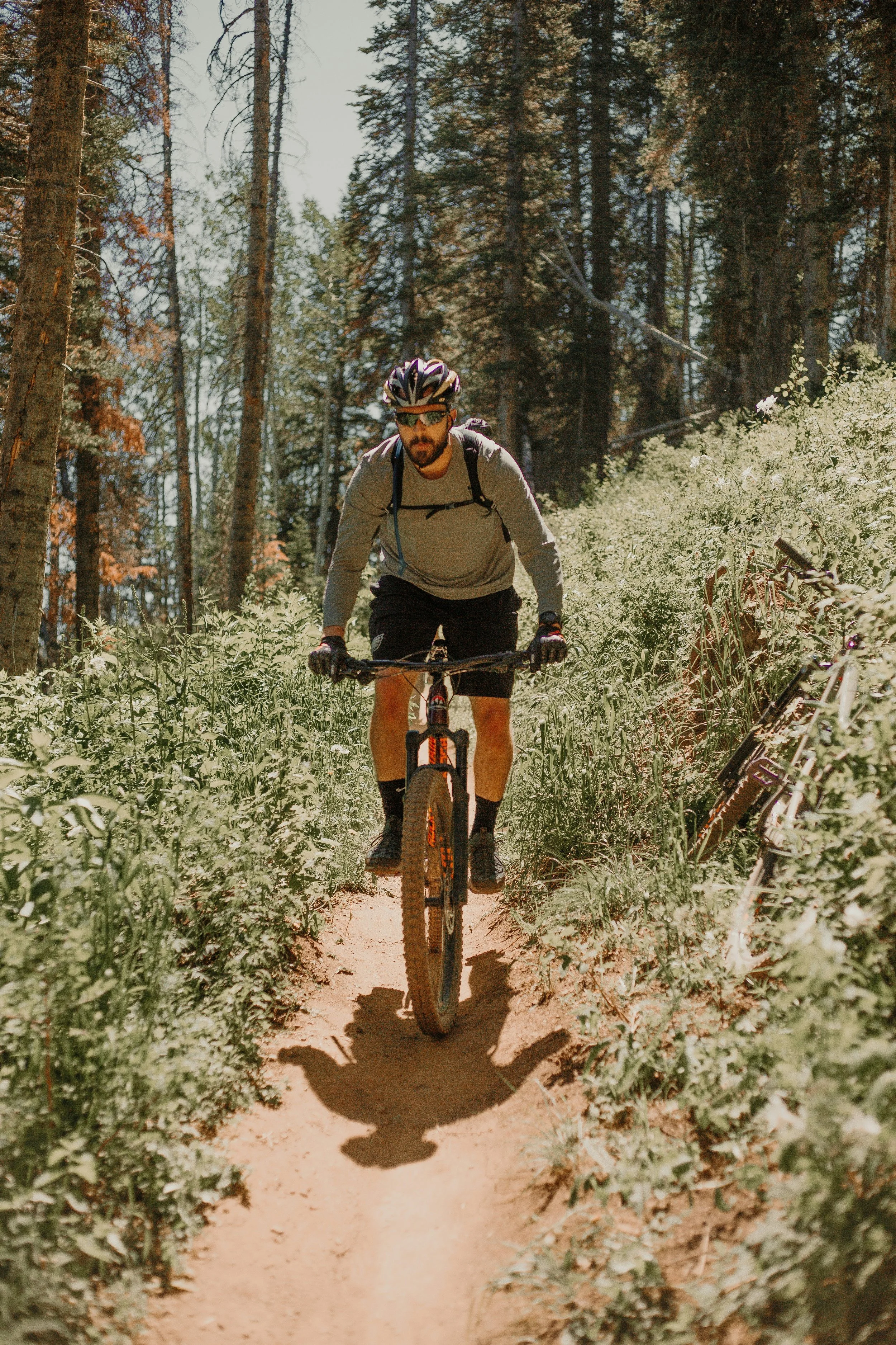 A man biking on a dirt trail in a forested area with tall trees and green foliage