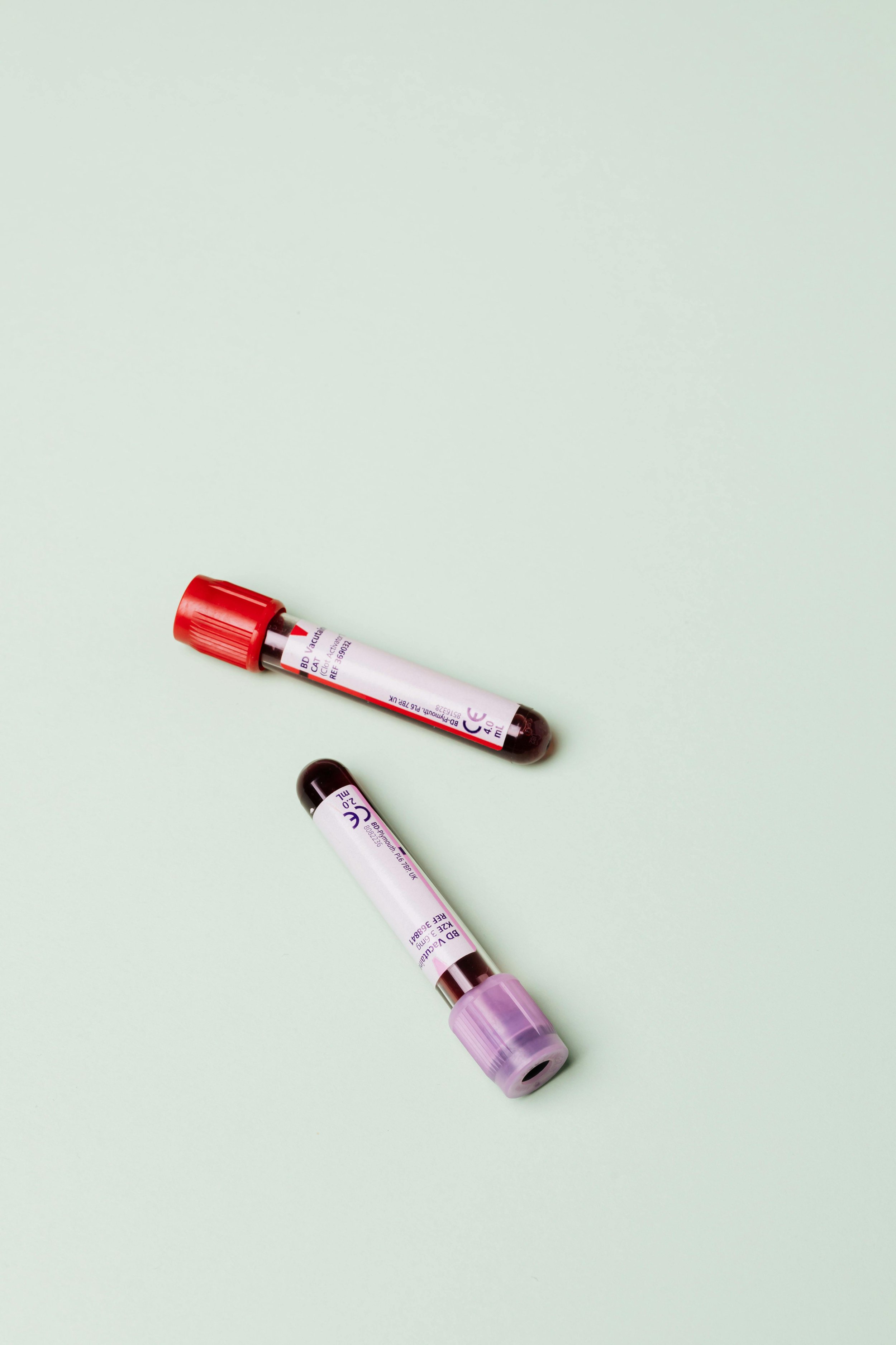 Three blood collection tubes with different colored caps lying diagonally on a light green background.