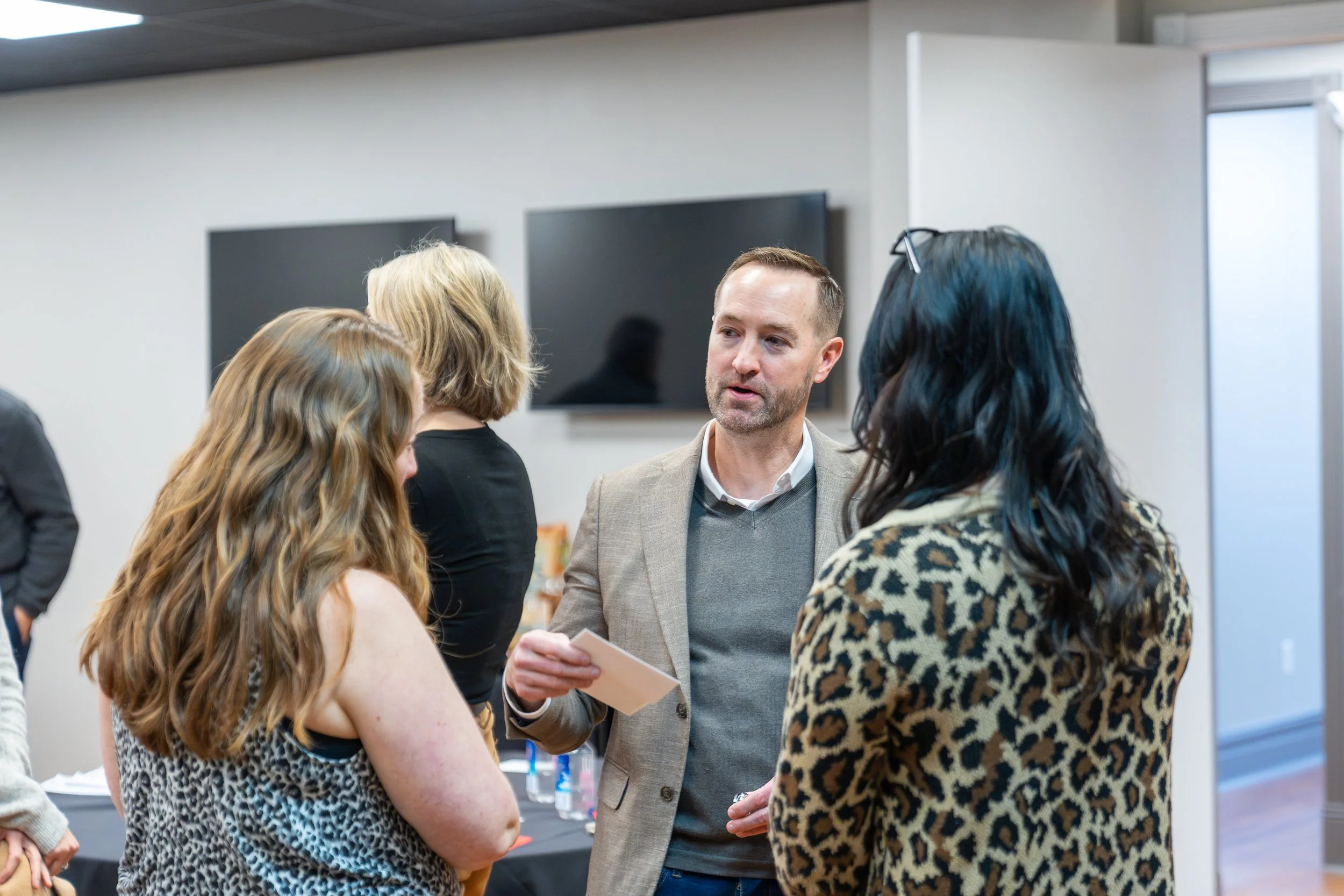 A group of four people engaged in conversation at a meeting or professional event in an indoor setting.