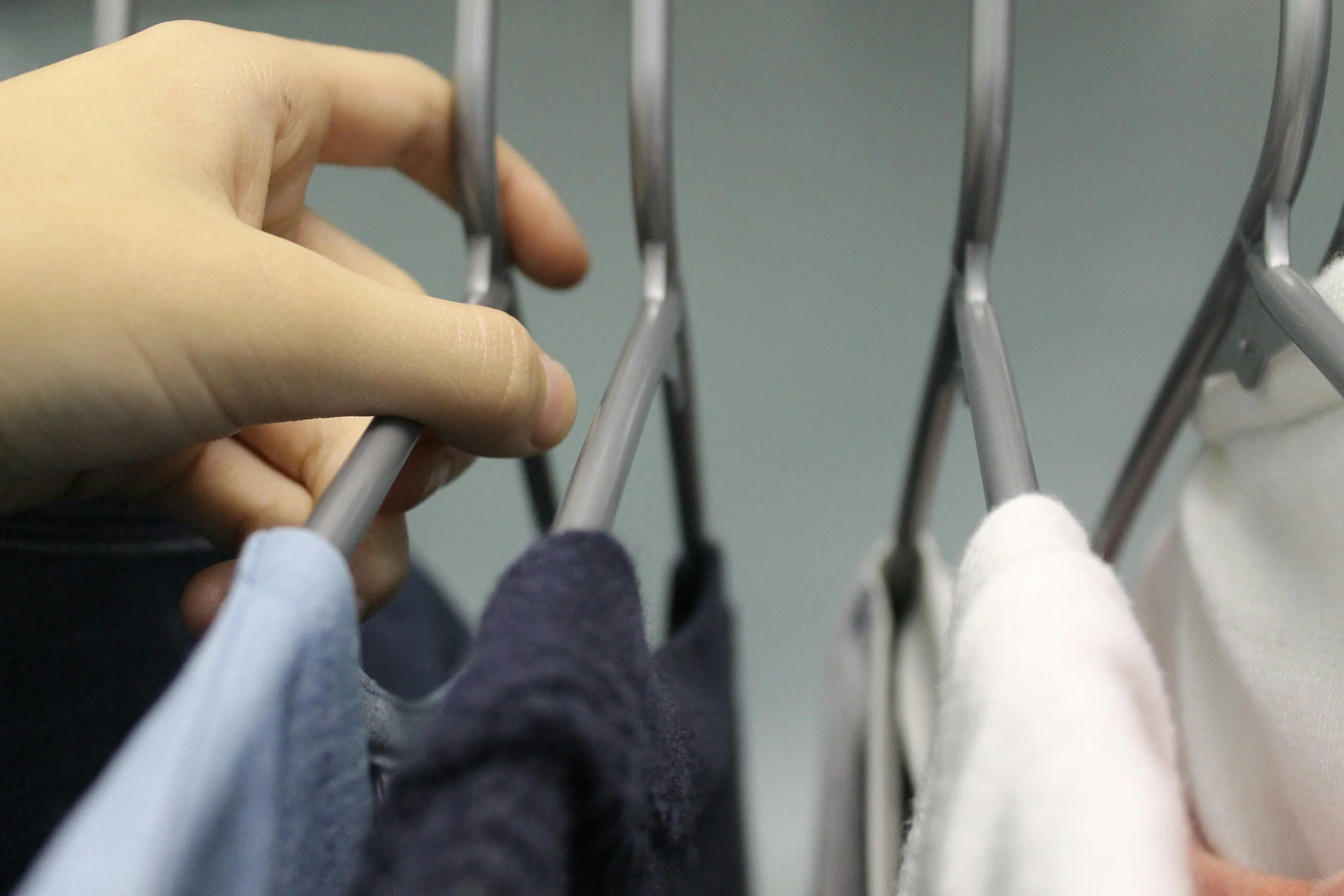 A person's hand reaching to hang clothes on a metal laundry drying rack.