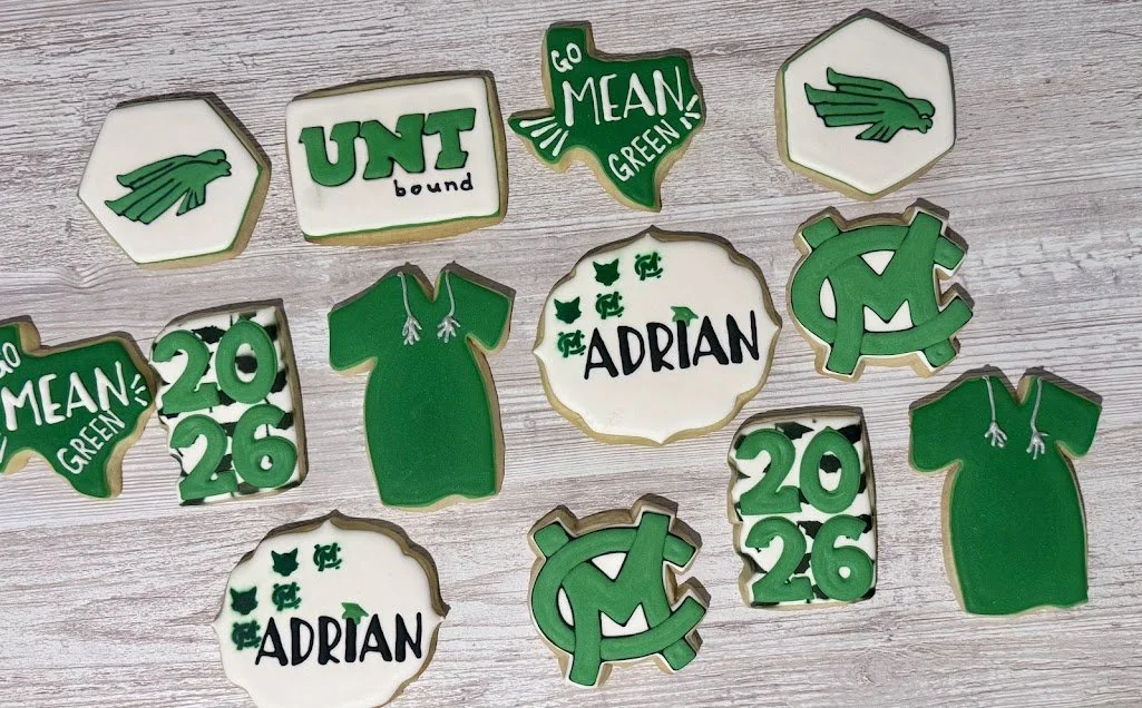 Collection of cookies decorated with green and white icing, themed around University of North Texas. Cookies include the UNT logo, a green shirt, the phrase 'Go Mean Green!', the year 2026, the name 'Adrian', and other university-related symbols.