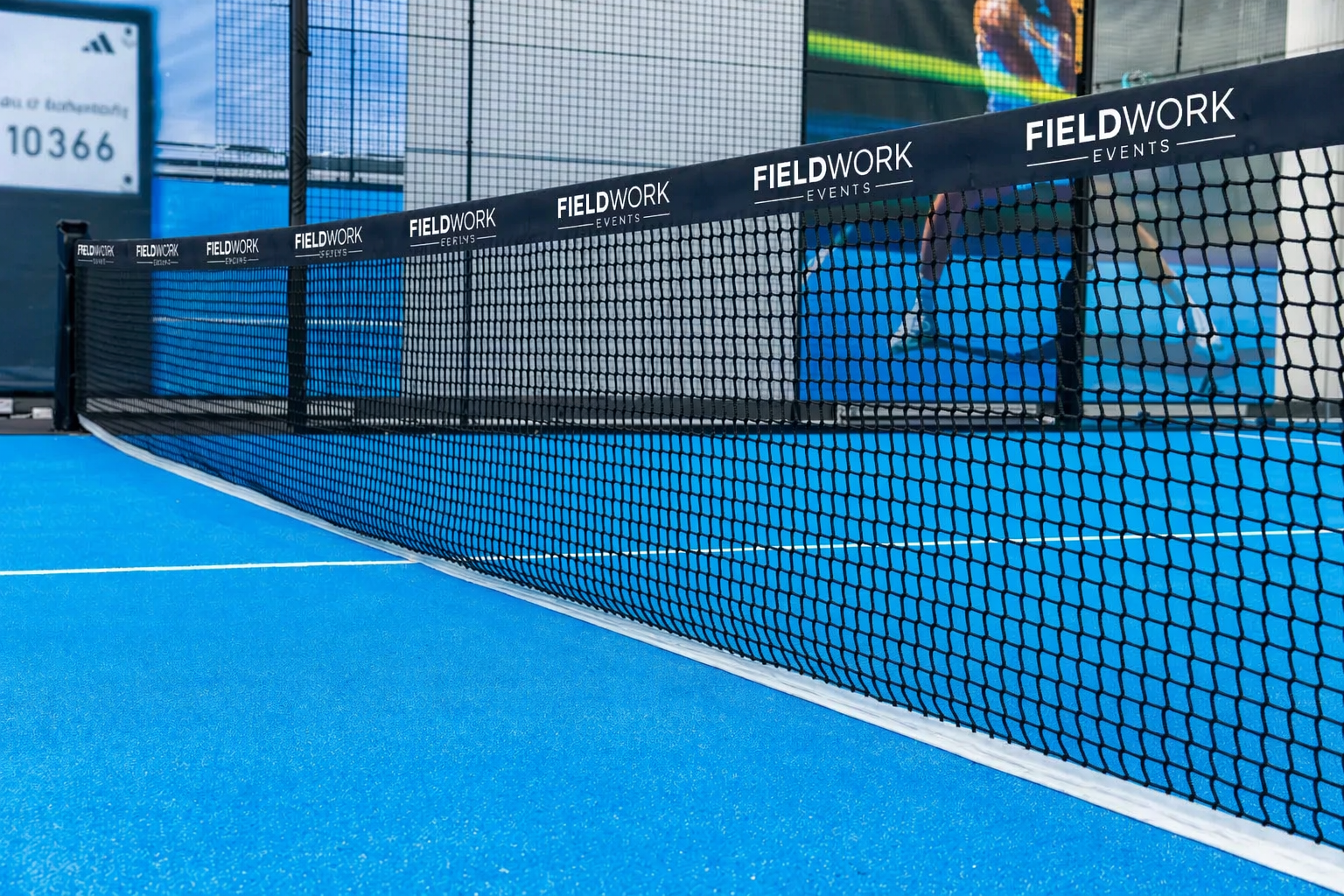 Close-up view of a tennis net on a blue court with advertisements that say 'FIELDWORK' and 'EVENTS'.