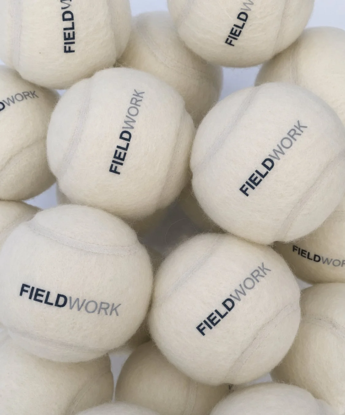 Close-up of several white felted wool golf balls with the word 'FIELDWORK' printed on them.