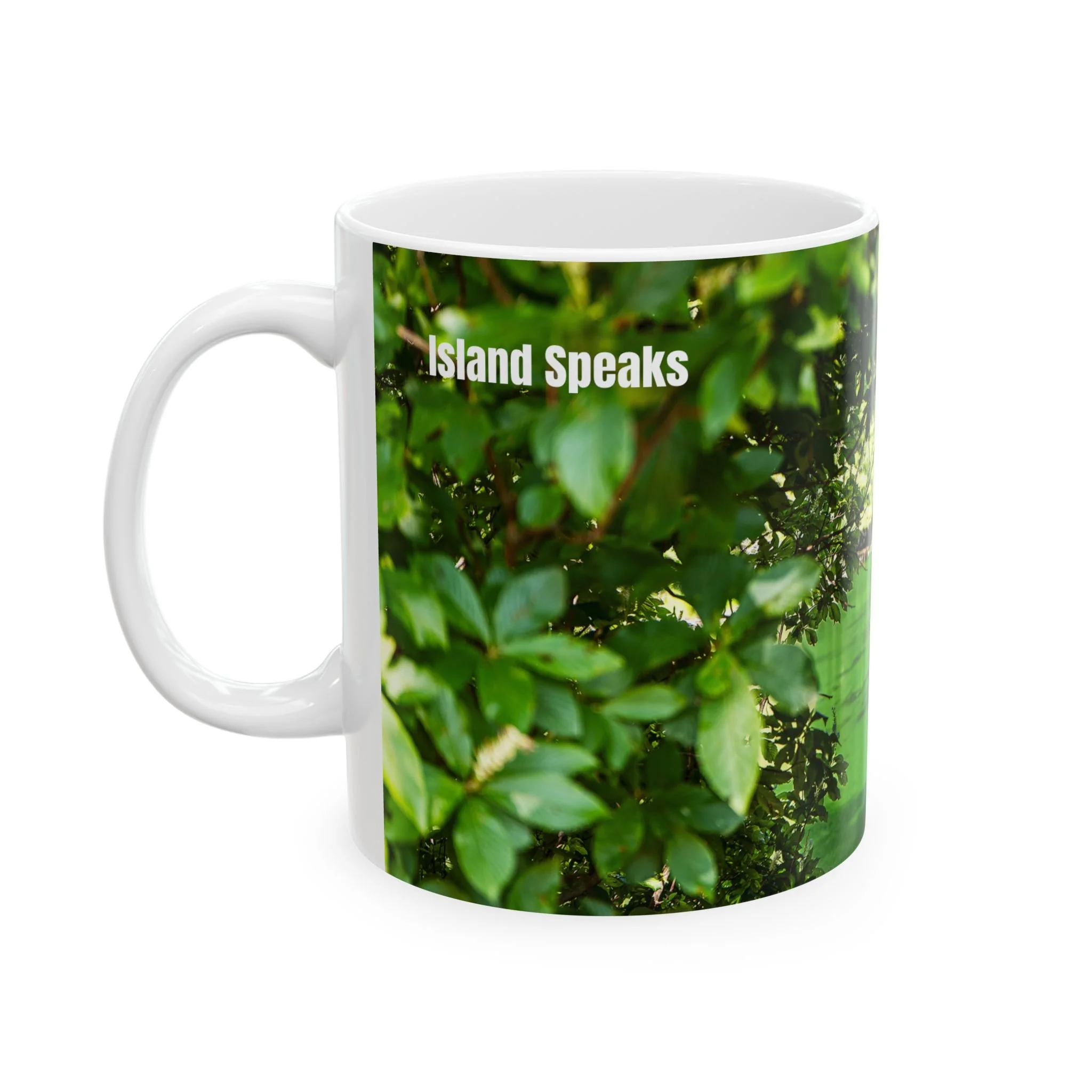 Island Speaks 'Portal Into the Lake' 11 oz mug product photo with left of mug showing. Left side of mug showing handle with part of photo on mug showing leafy green foliage and Island Auras brand name in white on top left of mug.