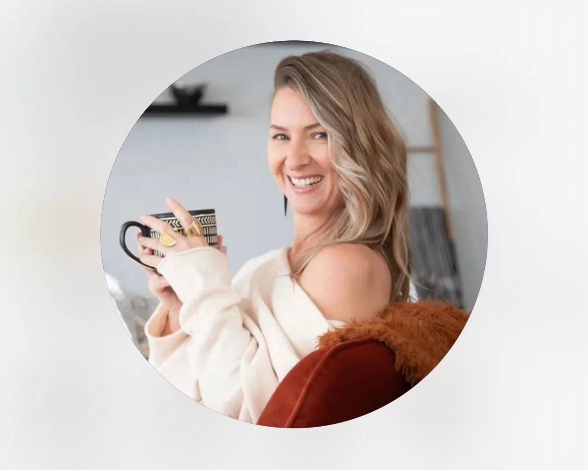 A smiling woman with blonde hair holding a coffee mug, sitting on a couch.