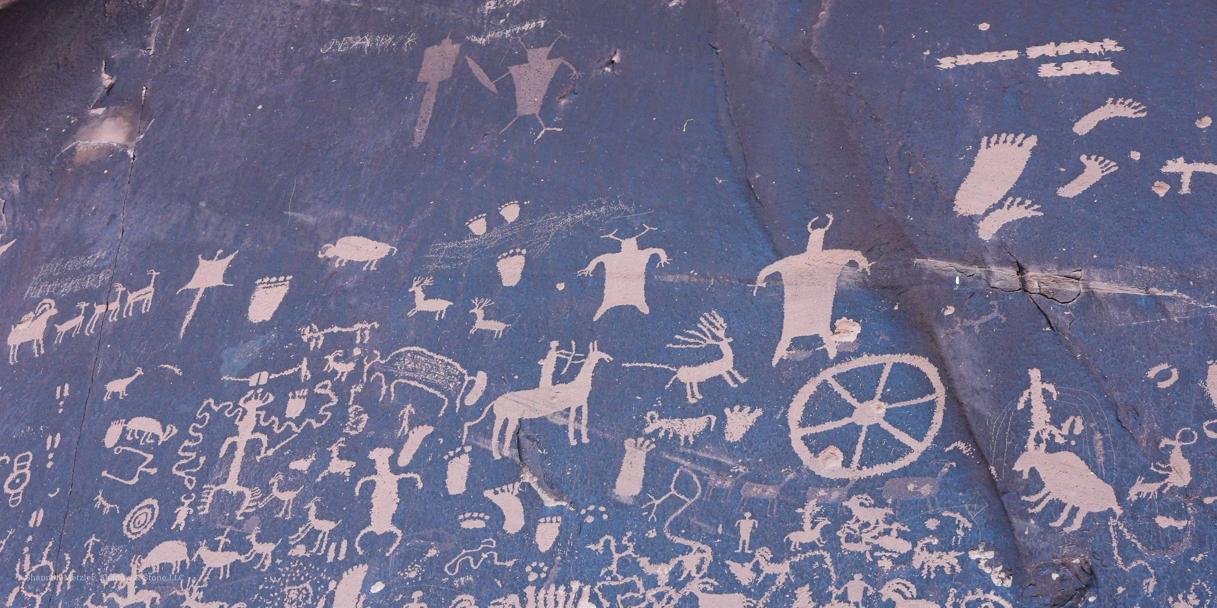 Ancient cave wall with petroglyphs depicting various animals, symbols, and human-like figures etched into the rock surface.