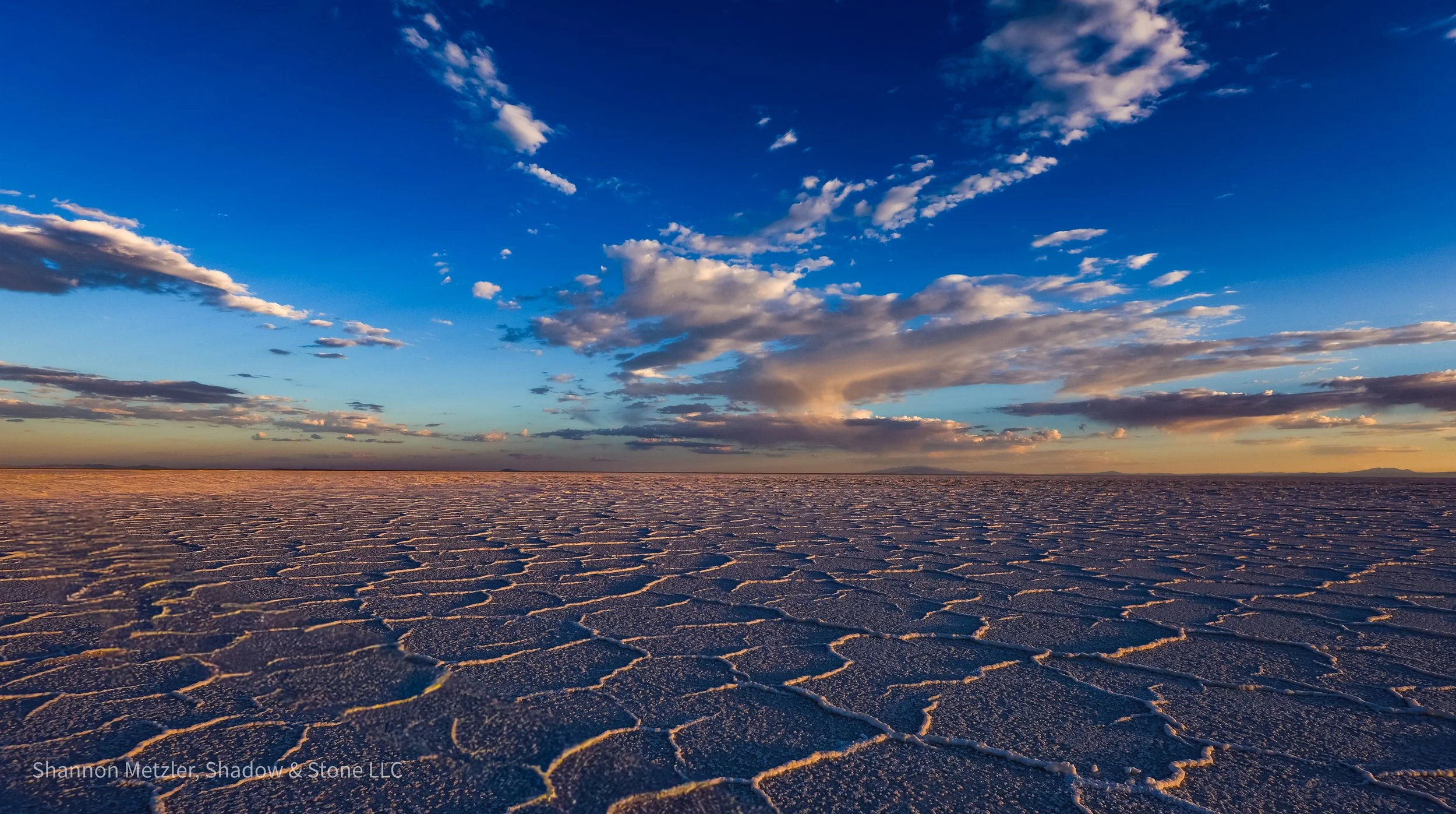A desert landscape with salt flats under a blue sky with scattered clouds at sunset.