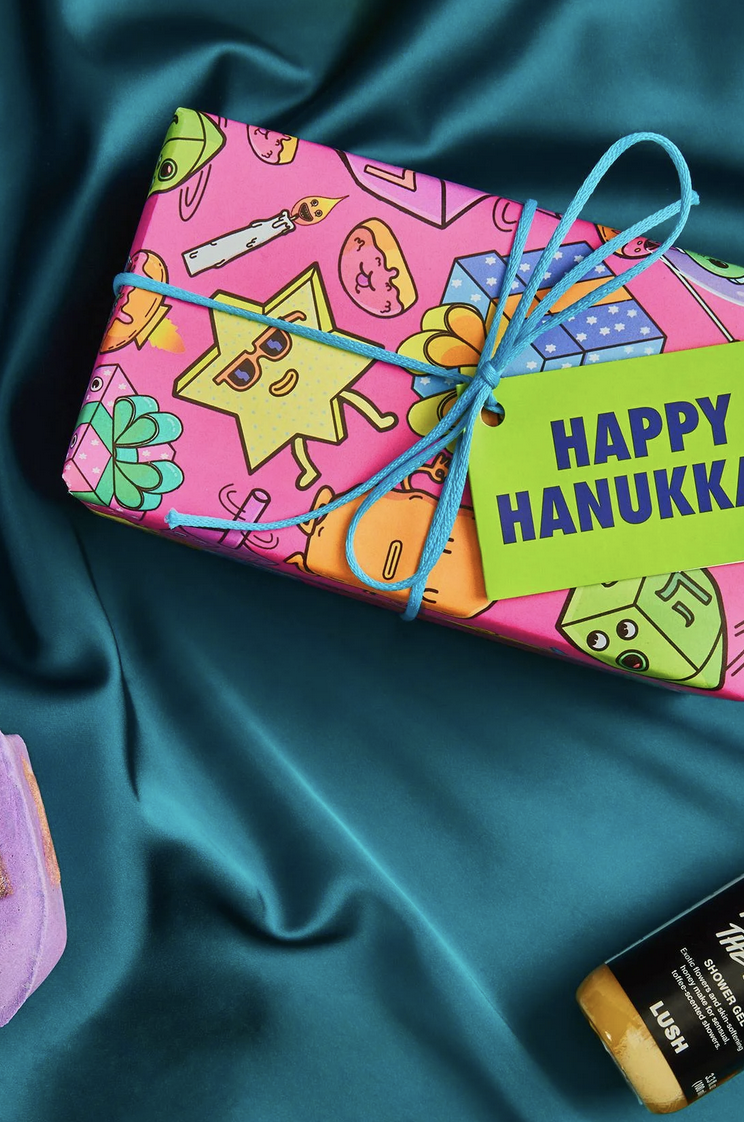Flat lay of Lush Soap's Happy Hanukkah Knotwrap fabric design by Danvillage — illustrated gift wrapping pattern with Jewish holiday characters and symbols