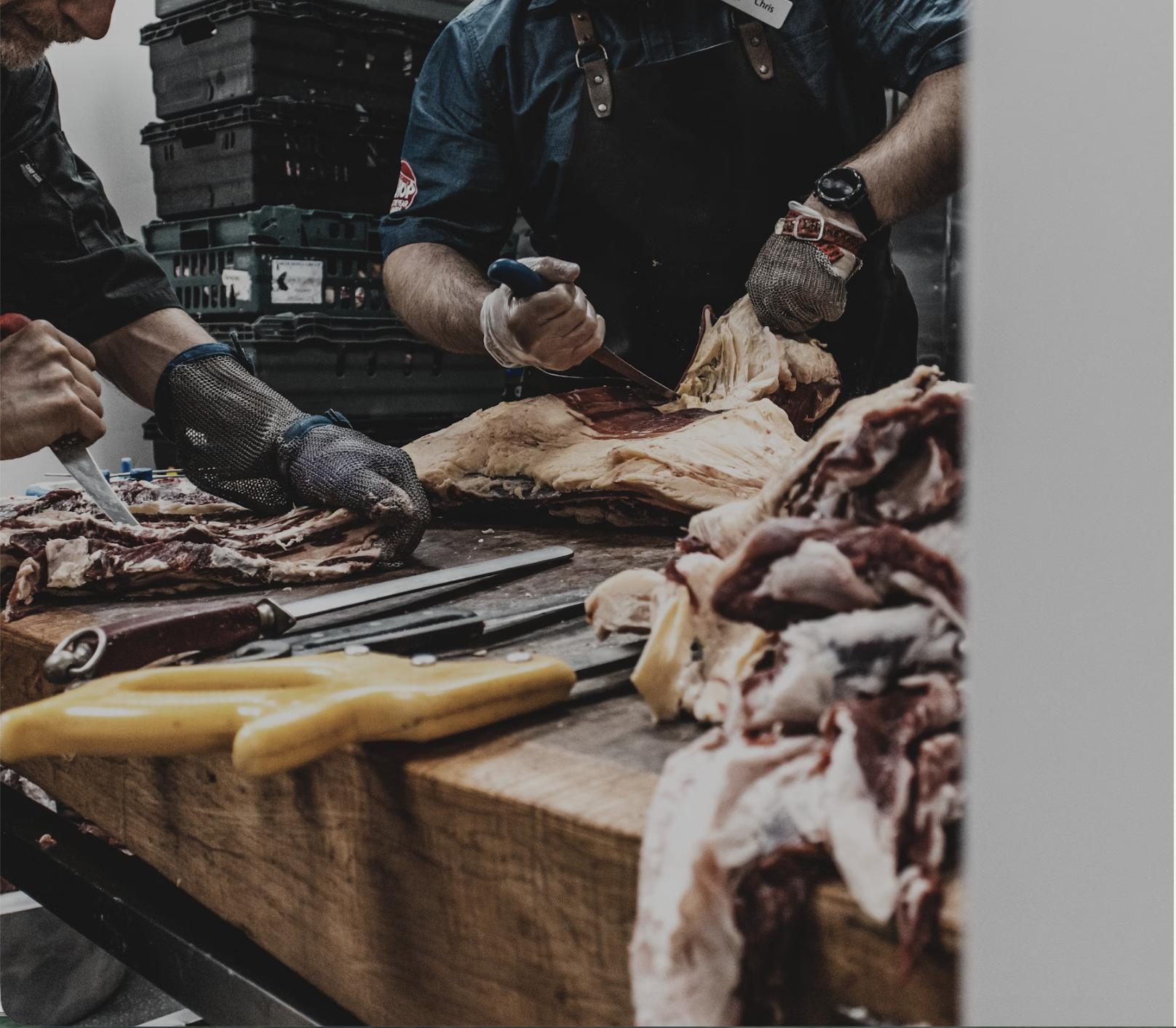 People butchering and preparing meat on a wooden table with various knives and meat cuts.