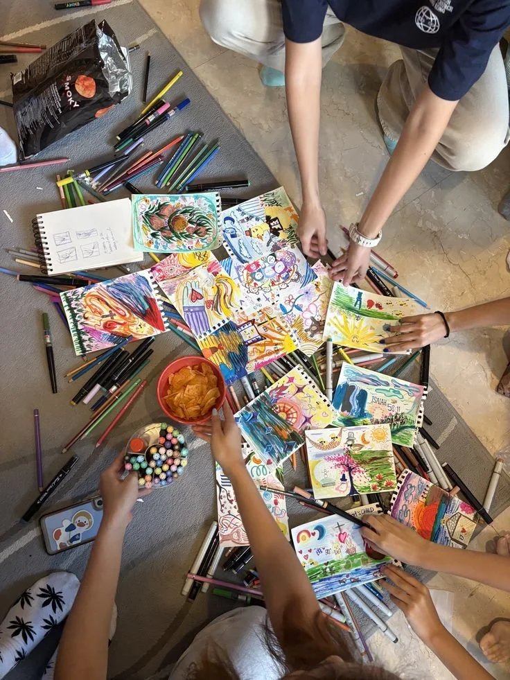 Children engaged in coloring and drawing colorful pictures on paper using markers and colored pens, with art supplies and snacks on a table.
