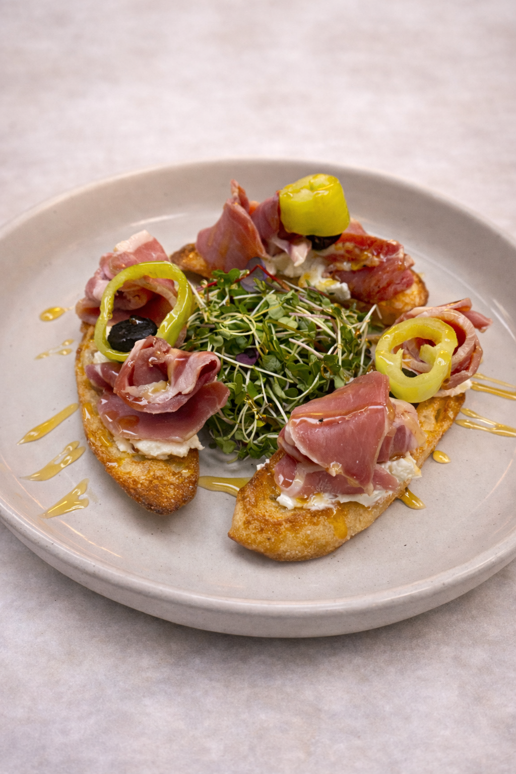 Cured ham, pepperoncini, black mission fig, over goat cheese on salted crostini with hot honey 