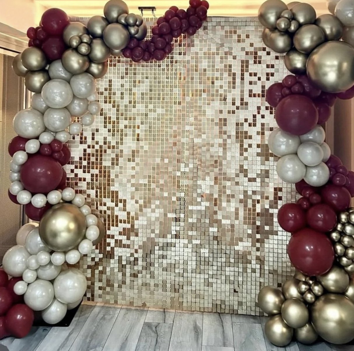 Decorative balloon arch composed of red, white, and gold balloons in front of a gold mosaic tiled backdrop.