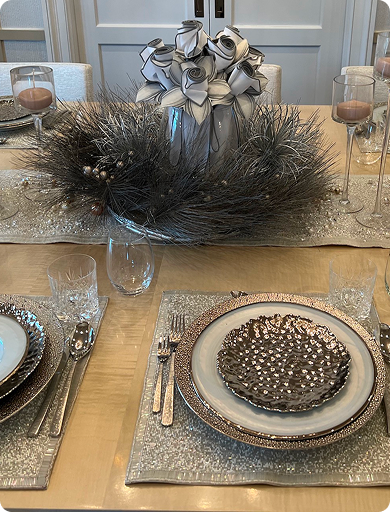 Decorative table setting with a centerpiece of black and white roses, black peacock feathers, and ornaments, with plates, glasses, and silverware arranged for a festive occasion.