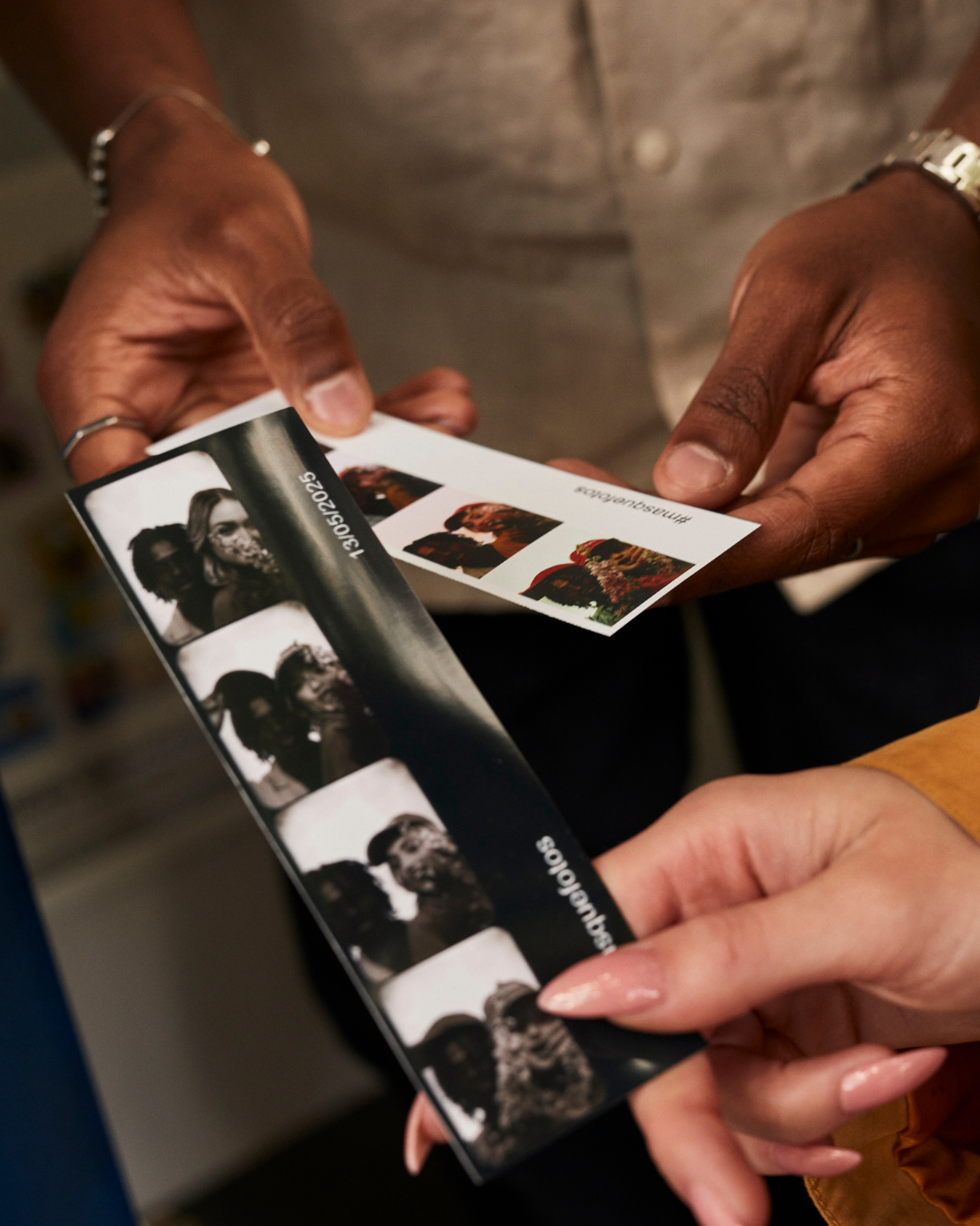 Close-up of two people exchanging a photo strip and individual photos, with various pictures of women, in a casual setting.