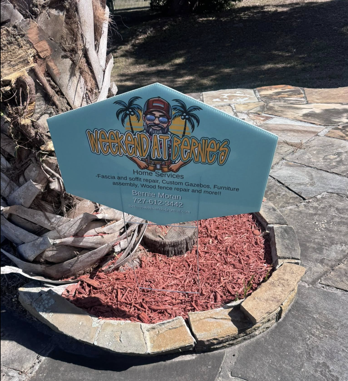 Sign advertising 'Weekend at Bernie's' home services, including fascia and soffit repair, custom gazebos, furniture assembly, and wood fence repair, with contact details for Bernie Moran.