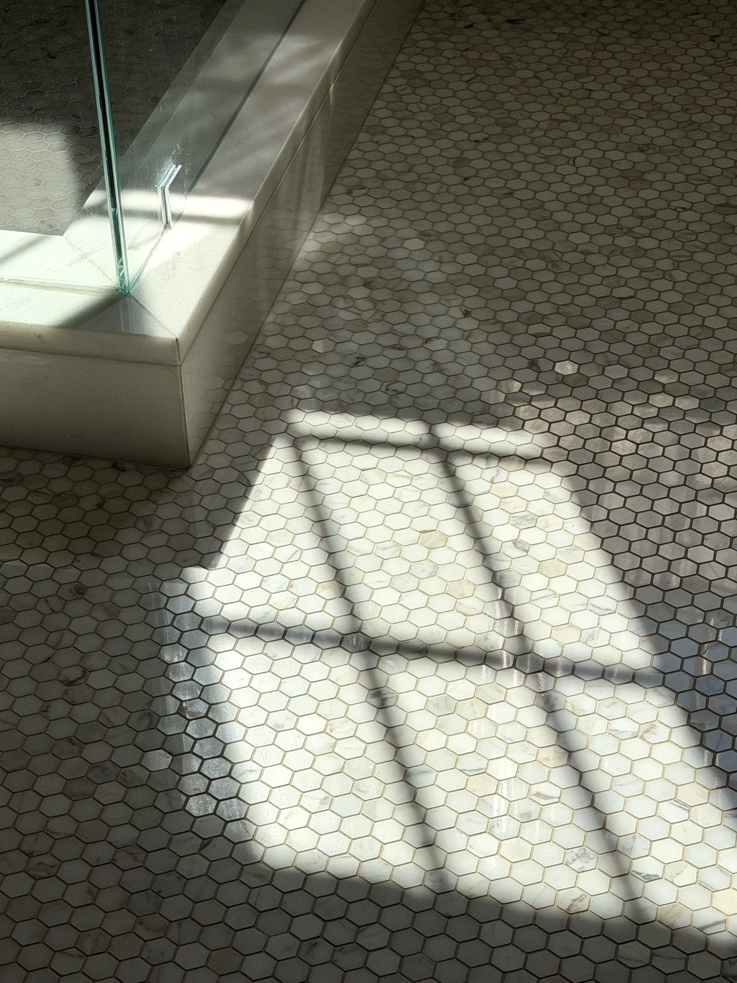 Sunlight casting shadows of a window frame on a tiled floor with hexagonal tiles.