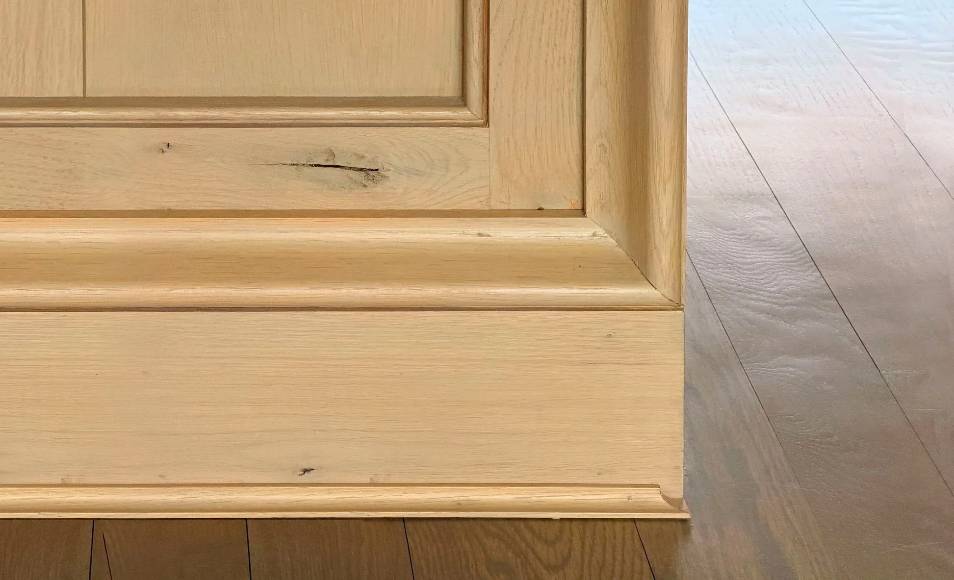 Close-up of light-colored wooden cabinet base and accent molding on a wooden floor.