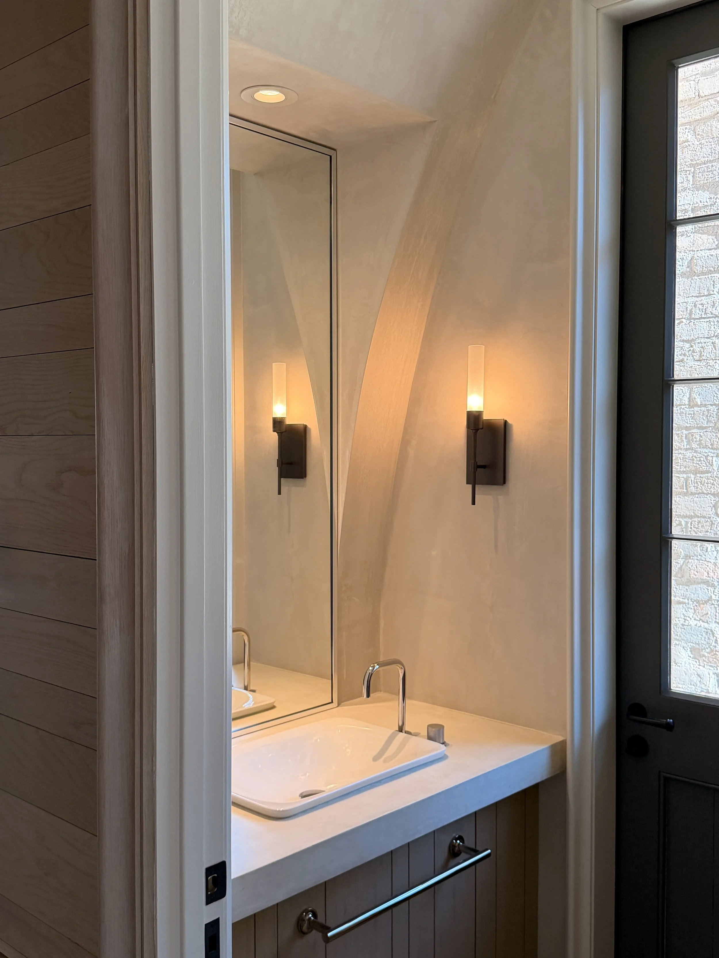 A bathroom vanity with a rectangular mirror, two wall-mounted light fixtures, a white sink with a modern faucet, and wood-paneled walls.