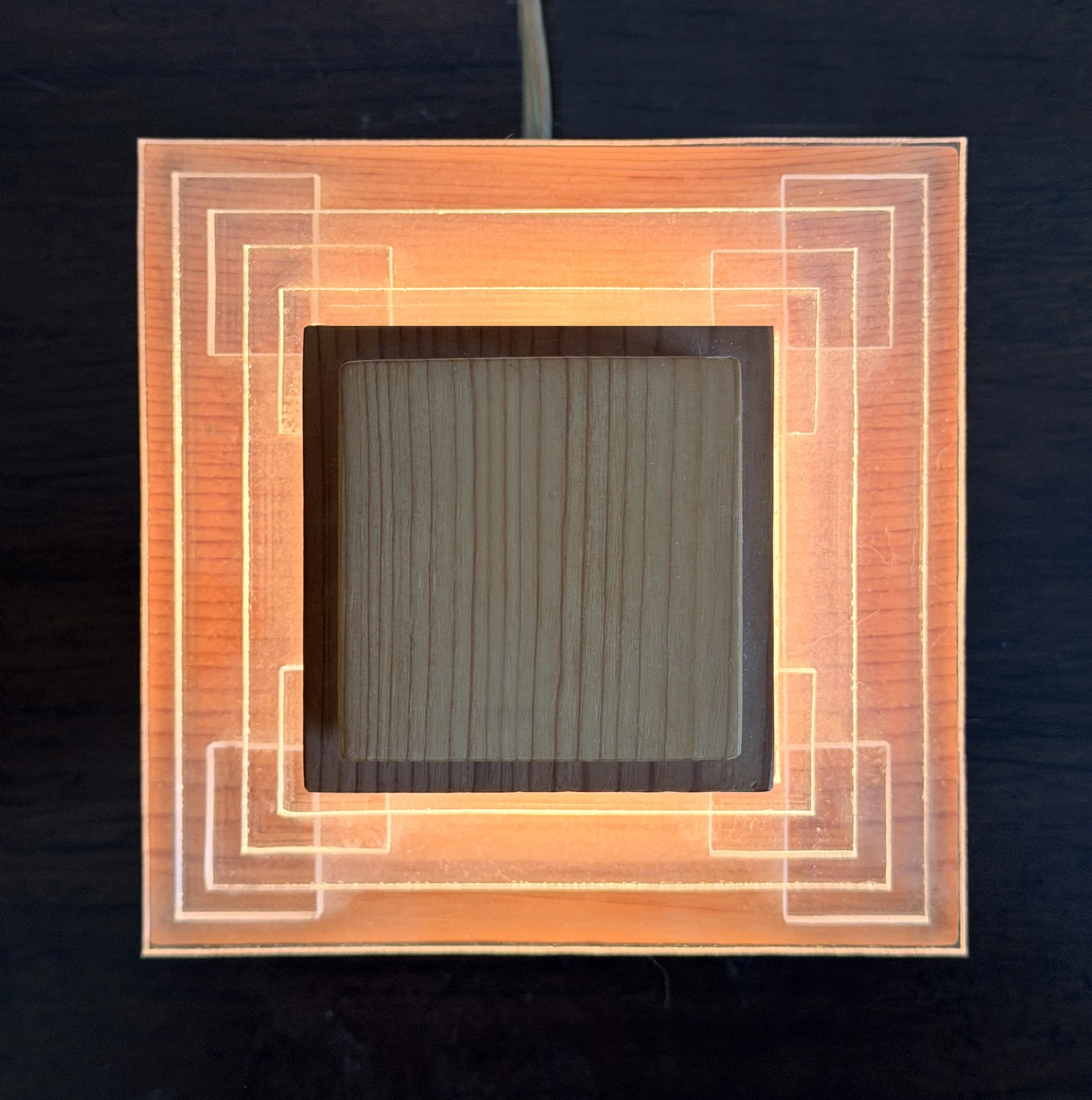Multiple wooden and transparent rectangular layers arranged in a geometric pattern on a dark surface.
