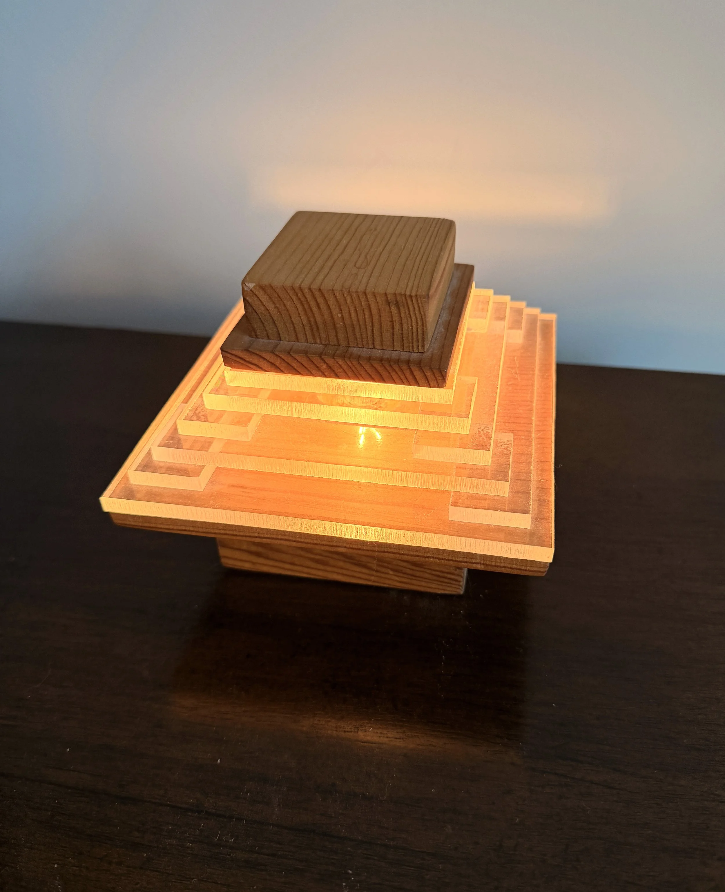 Stacked wooden blocks with a warm light illuminating the top block, placed on a dark surface against a plain background.