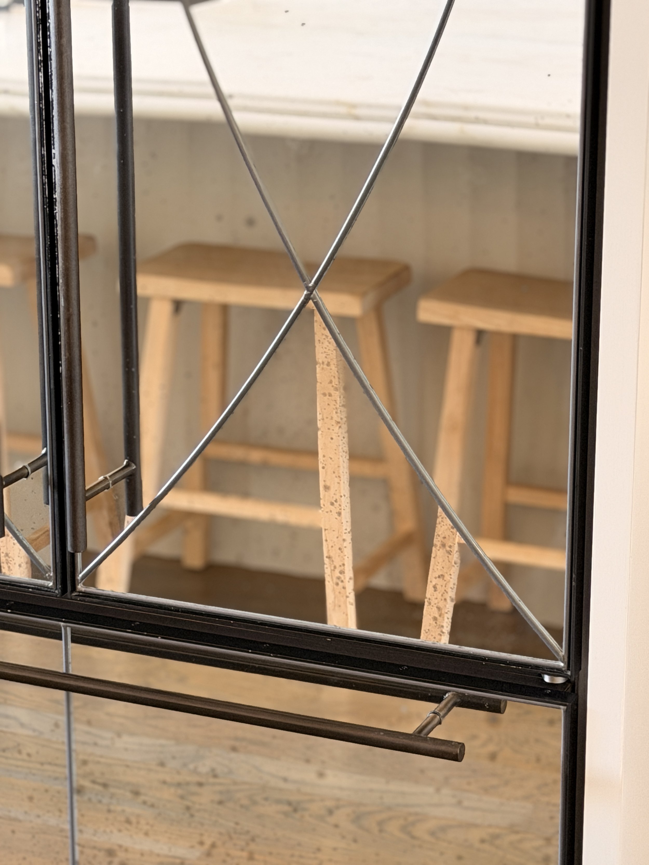 Close-up of a black metal and wire shelf with a wooden stool and a white surface in the background.
