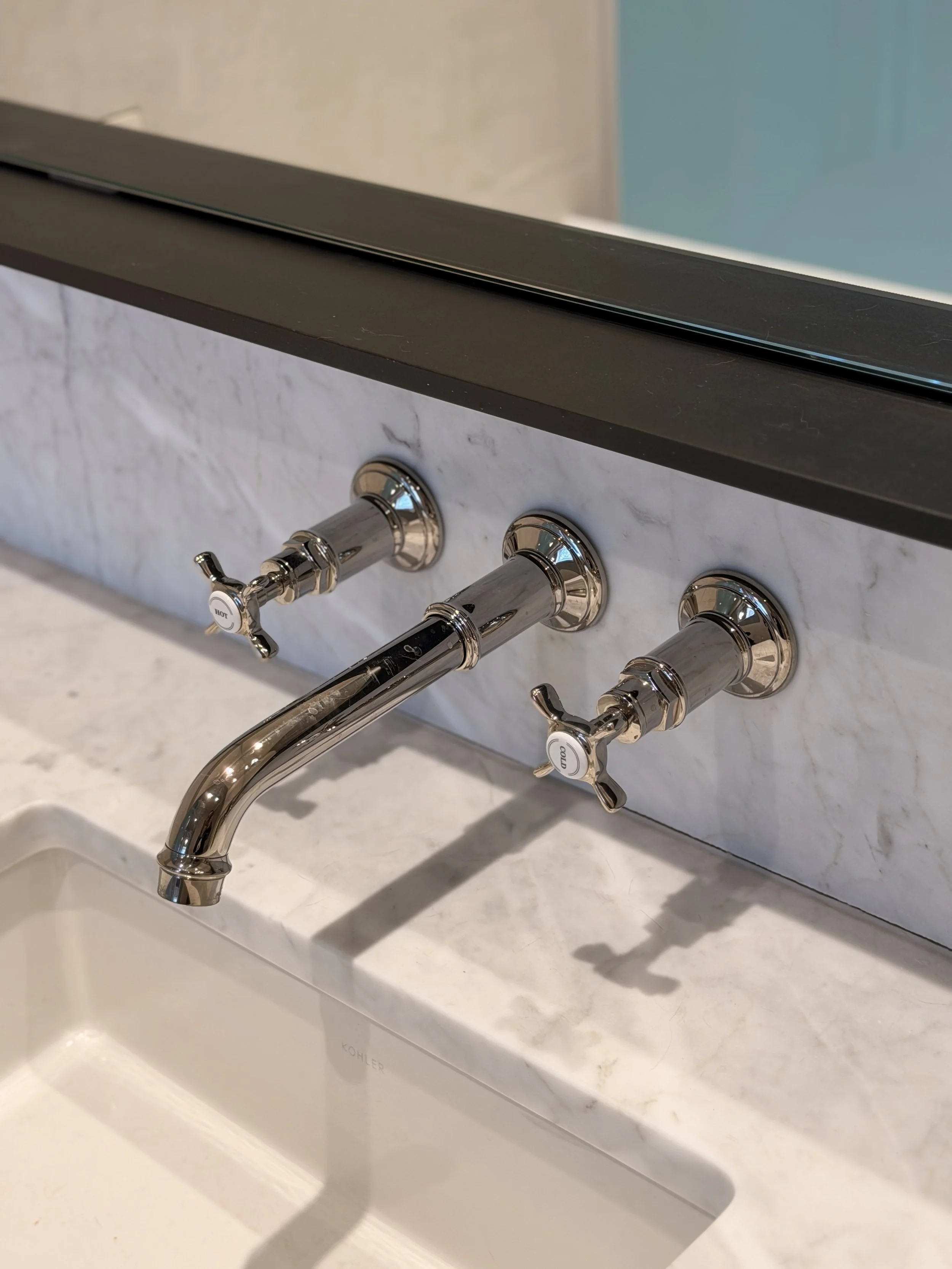 Close-up of a modern kitchen faucet with a marble countertop and backsplash.