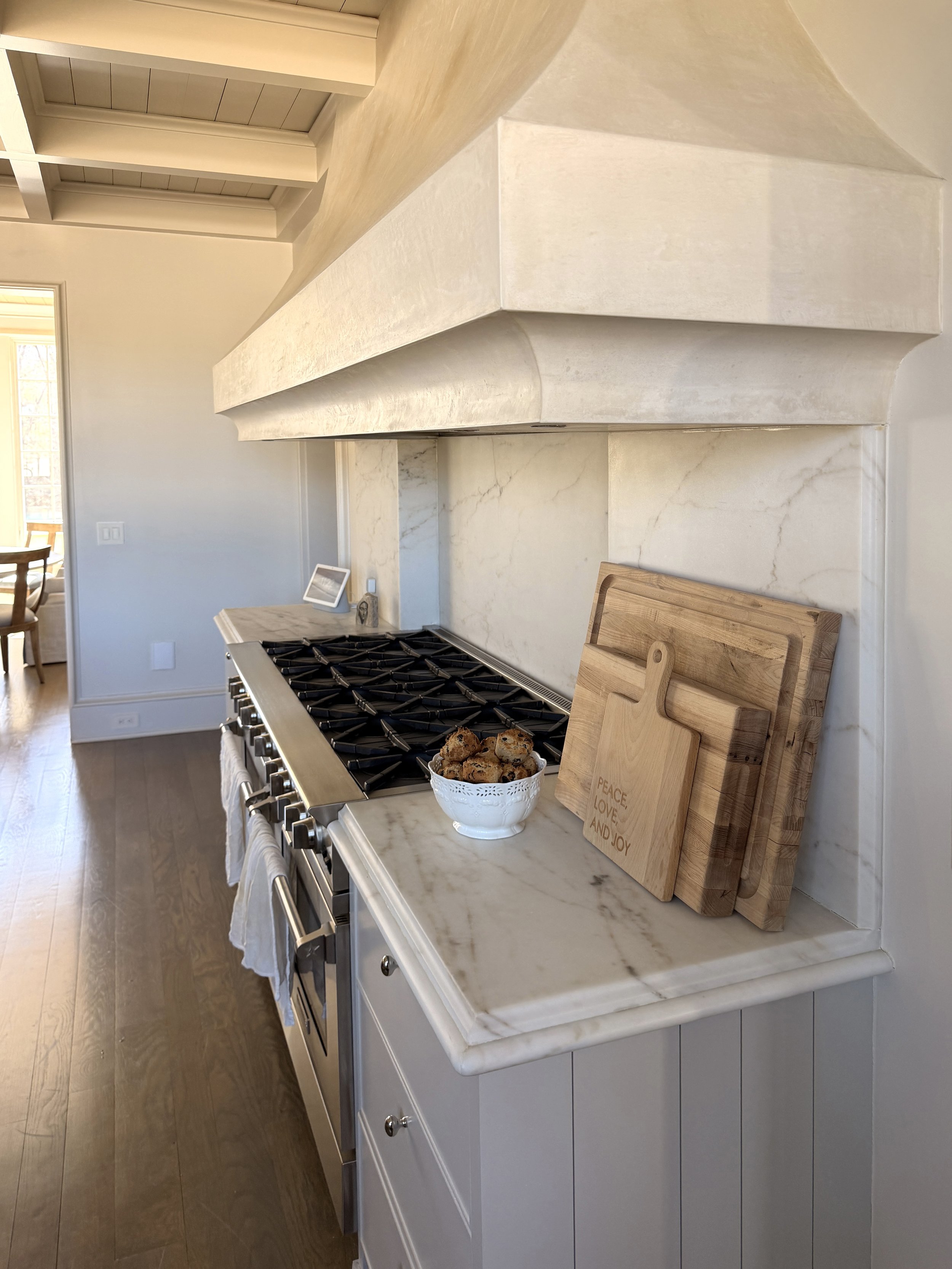 Kitchen with marble countertop, wooden cutting boards, bowl of cookies, and stove, in a well-lit room with hardwood floors.