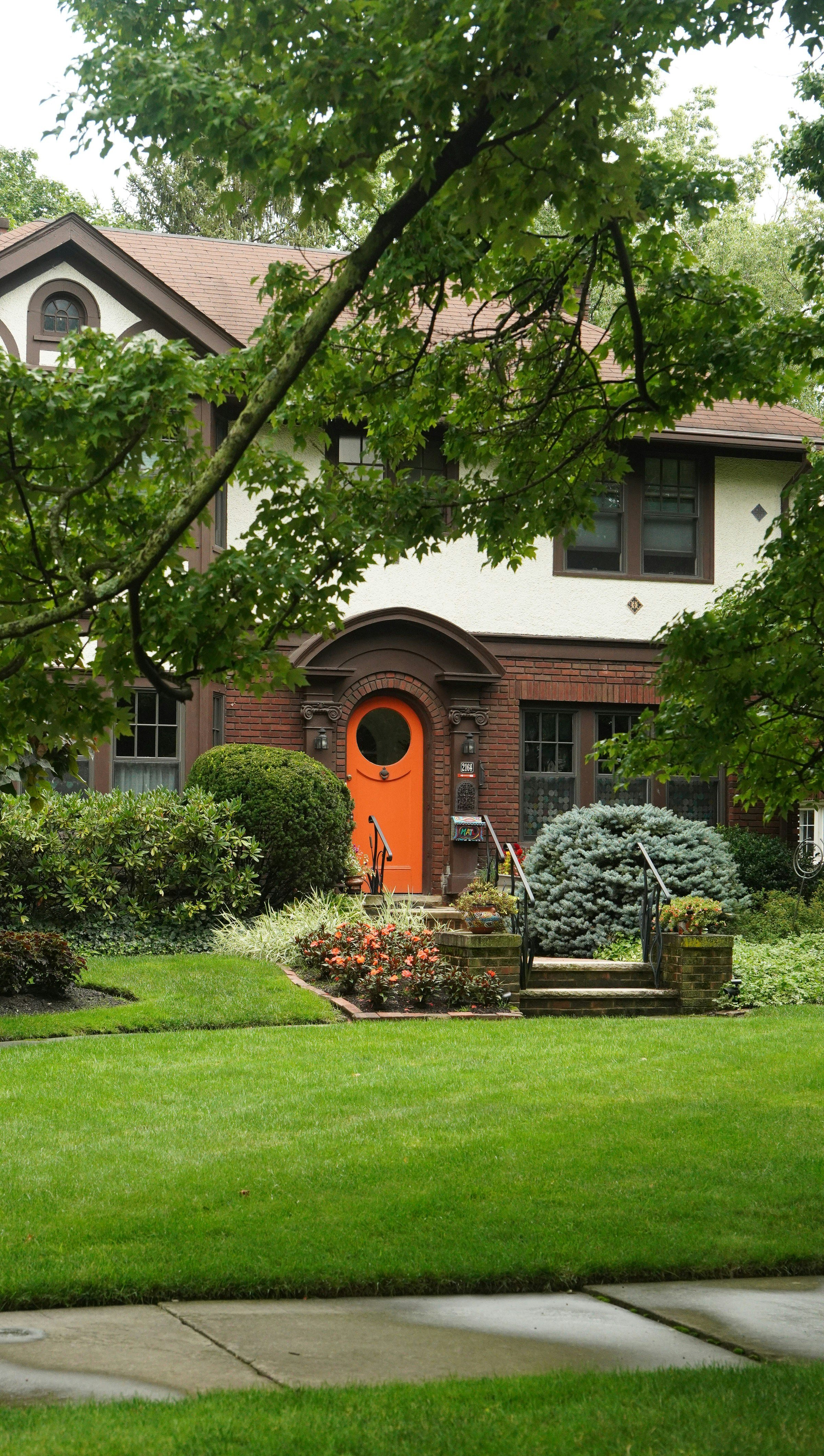 A rustic, cottage-style house with a vibrant green lawn, orange flowers, and orange door, and a brick stoop, showing finely cut lawn by BlockMow