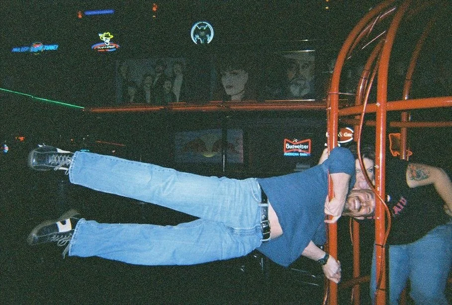 Vic Alejandro horizontally balanced and extended from a pole of a cage in a bar. 
