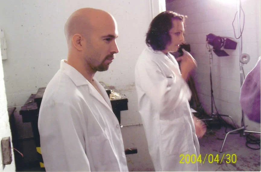 Vic Alejandro and Richard Greico in white lab coats standing in a room with medical or scientific equipment. It is a picture from the set of the "Raiders of the Damned" movie. The picture is dated April 30, 2004.