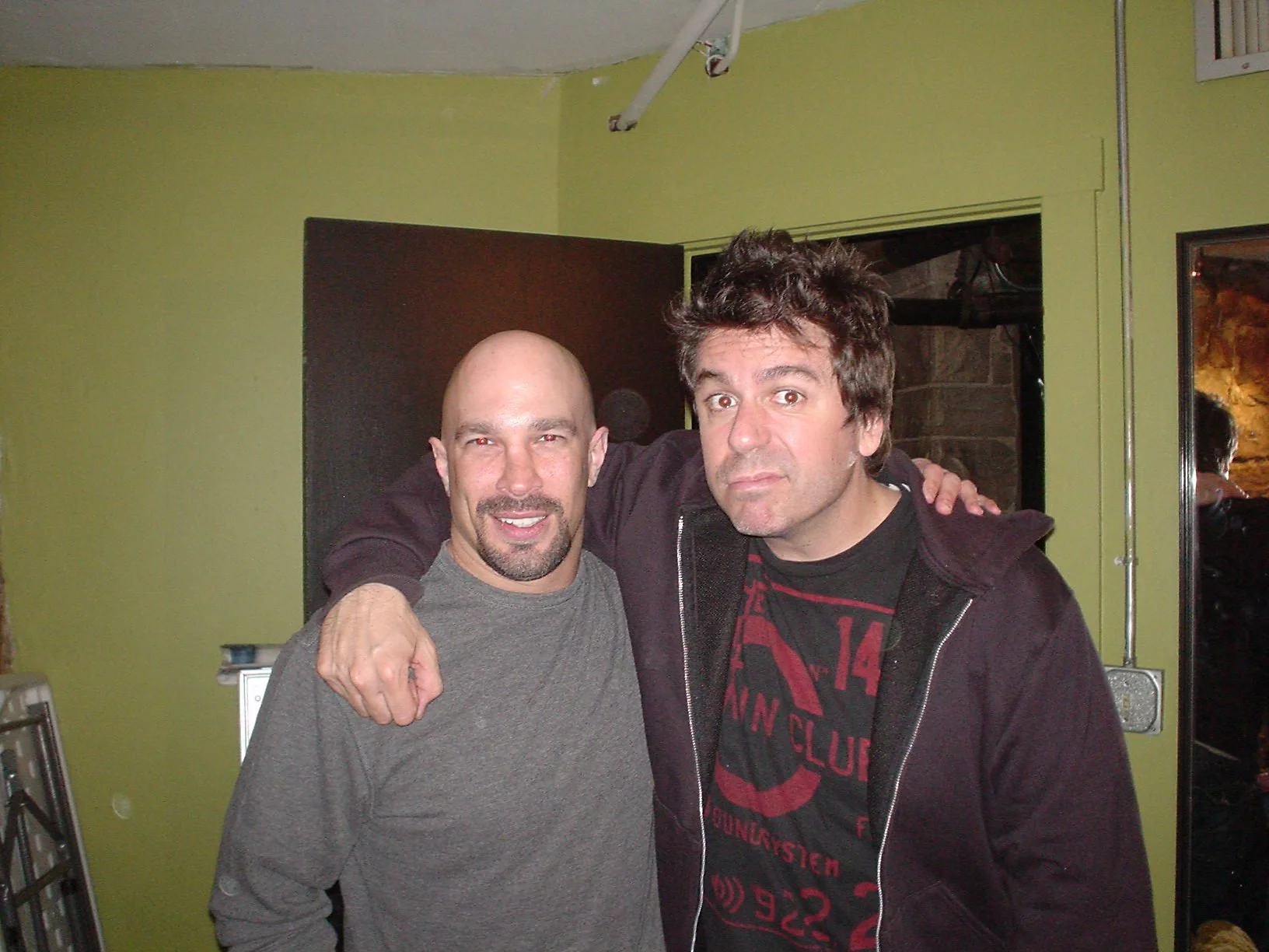 Vic Alejandro with comedian Greg Giraldo (RIP) in the green room of Comedy Works in downtown Denver, Colorado. Two men standing close together with their arms around each other, smiling, inside a room with light green walls.
