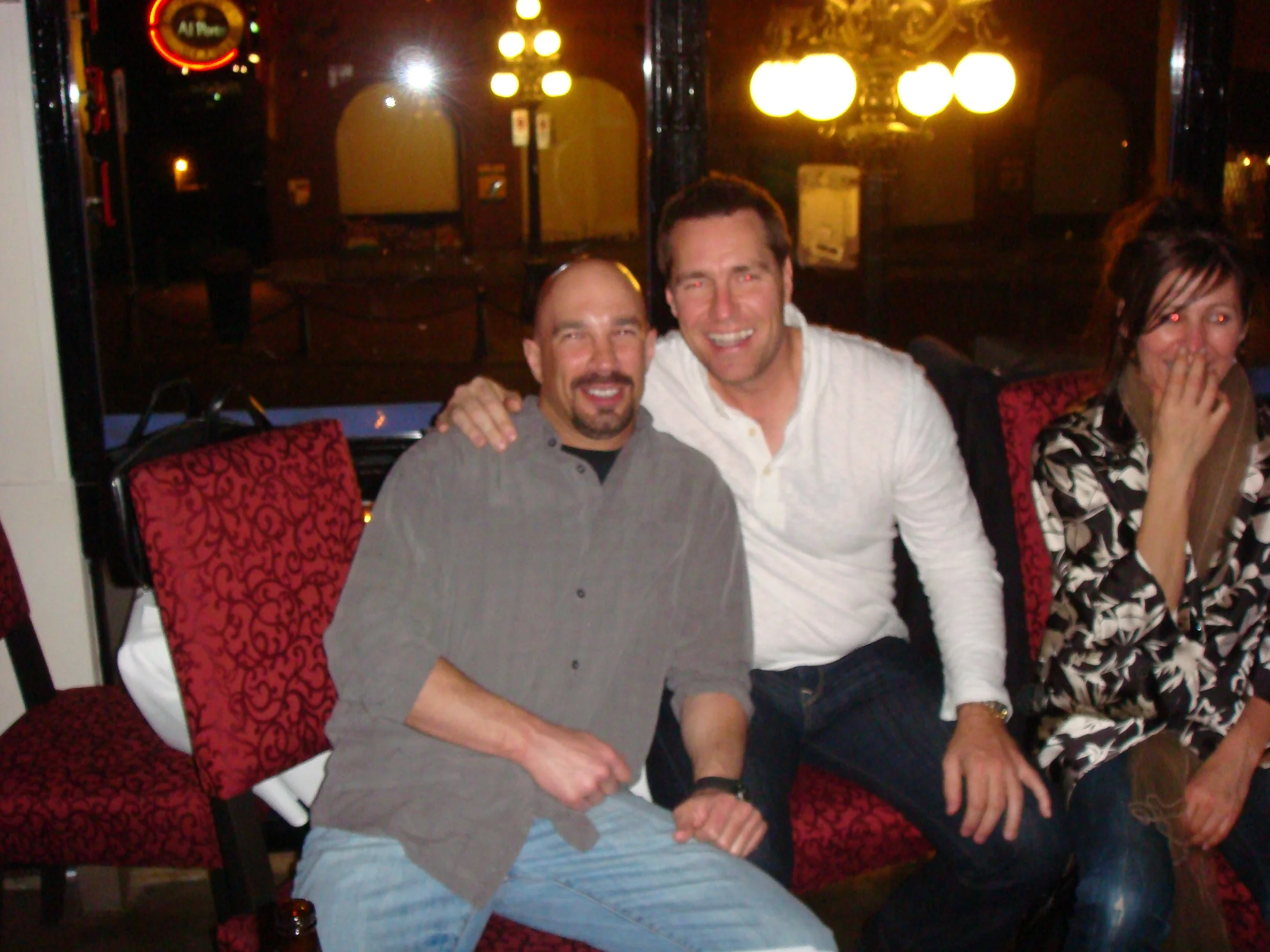 Vic Alejandro with former NHL goalie Kirk McLean sitting on red patterned chairs, smiling and posing for a photo in a bar in Edmonton, Alberta.