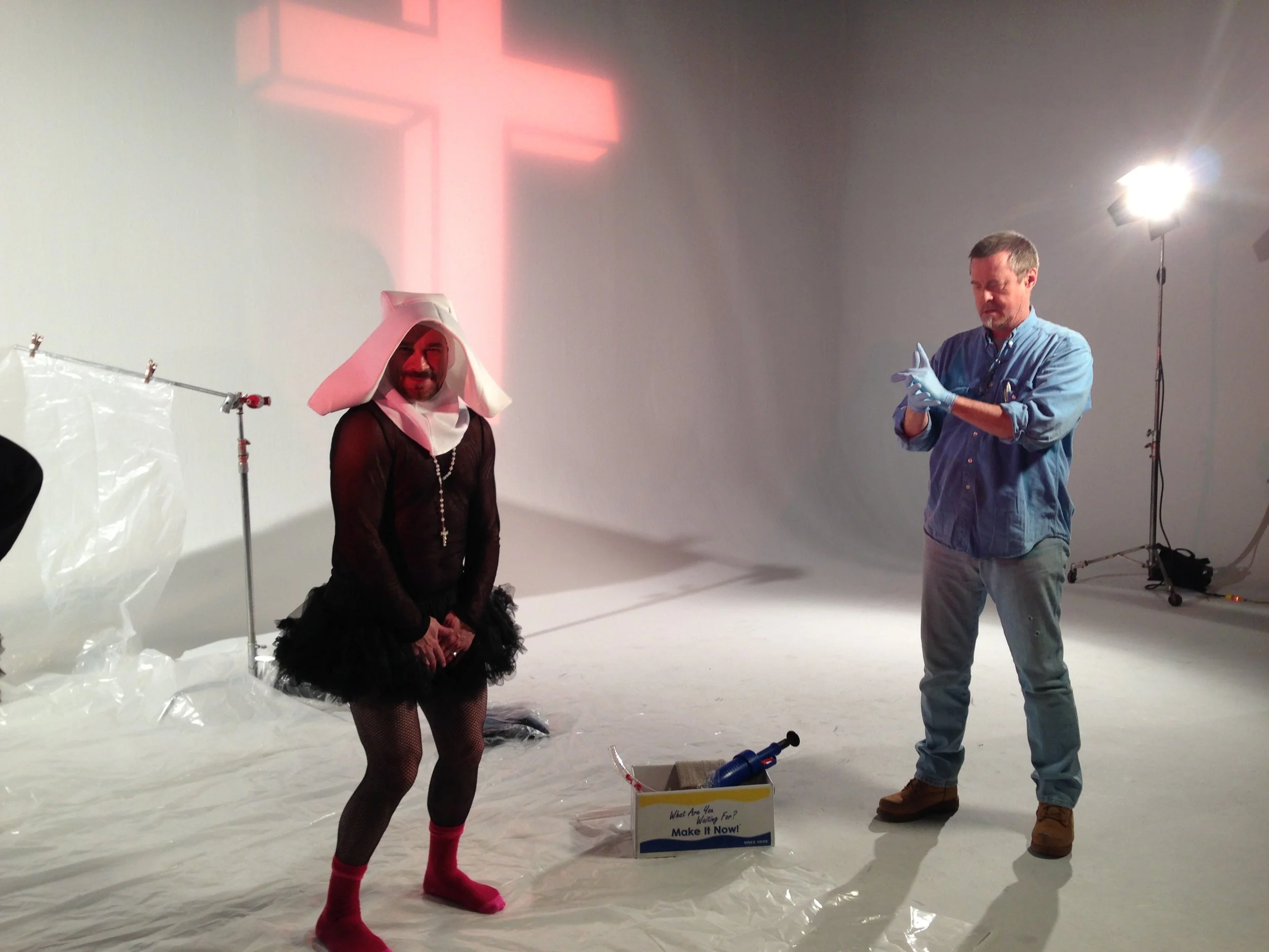 Vic Alejandro on the set of "Directors on Directing" dressed as a nun in a white habit and black tutu skirt. There is a tech person standing in front of him ready to blast him with fake blood for a scene.