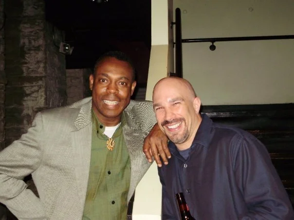 Vic Alejandro with comedian Michael Winslow (the guy that does the noises in Police Academy) in the green room of Comedy Works in downtown Denver, Colorado. Two men smiling and standing close together indoors with brick walls.