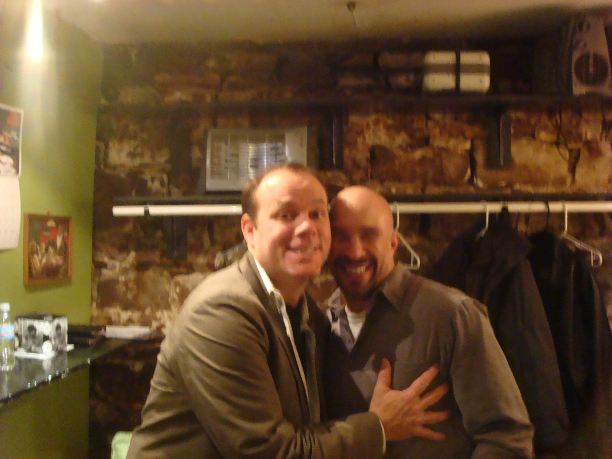Vic Alejandro with comedian Tom Papa in the green room of Comedy Works in downtown Denver, Colorado. Smiling and posing together with Tom groping Vic's breast in front of a brick wall background.