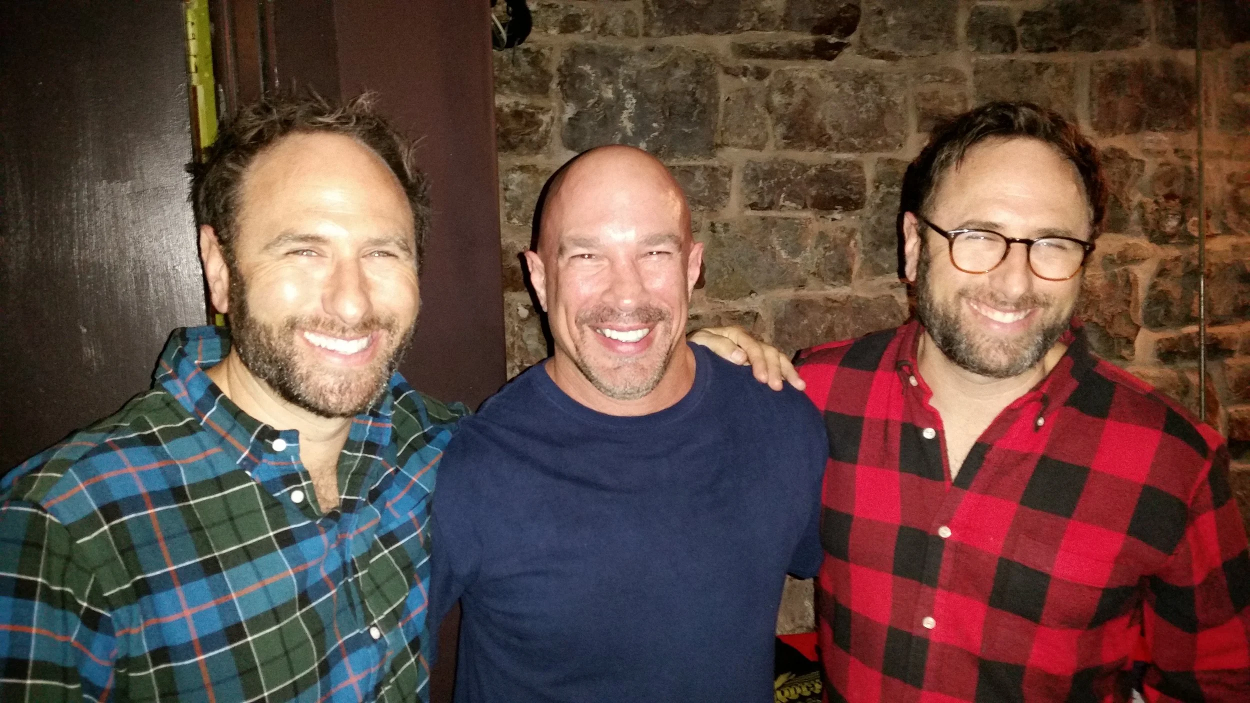 Vic Alejandro with the Sklar Brothers in the green room of Comedy Works in Denver, Colorado. The men are smiling, standing close together, with casual clothing and a brick wall background.
