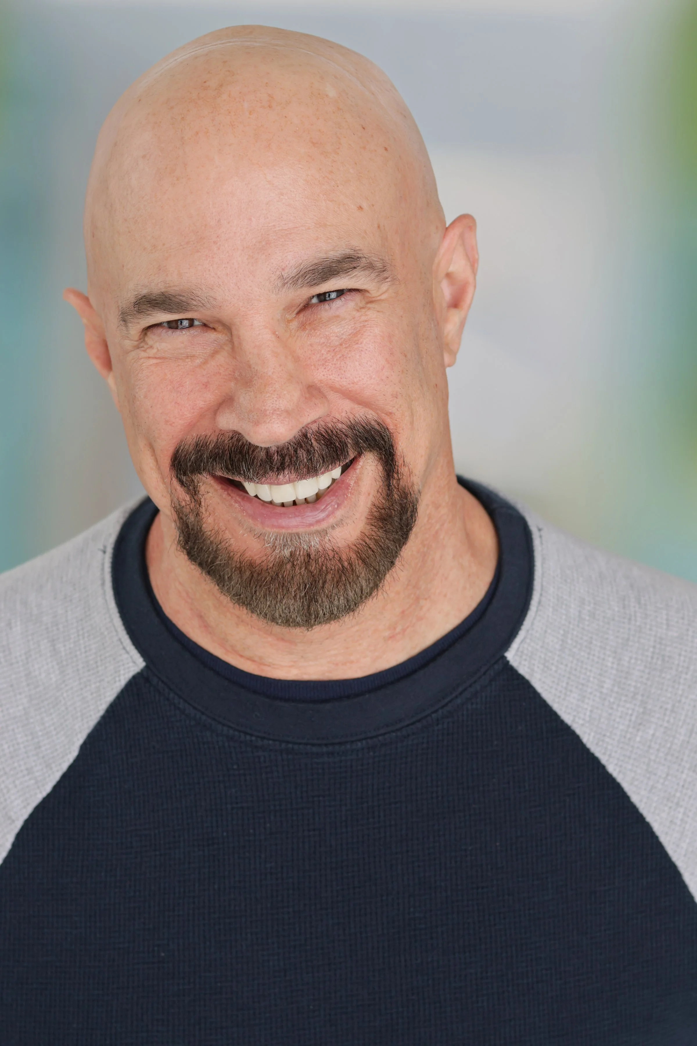 Vic Alejandro smiling with a bald head, a mustache, and a goatee wearing a gray and navy blue sweatshirt.