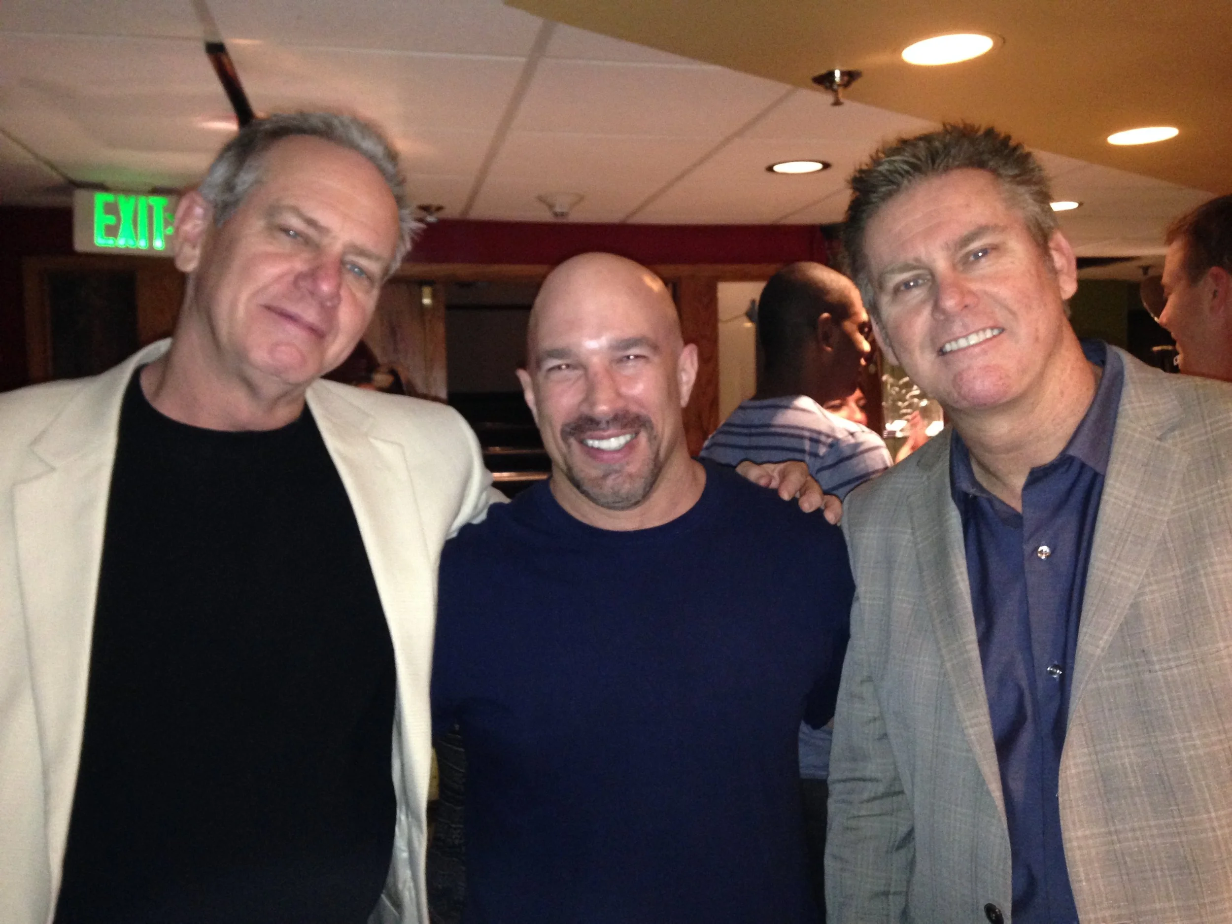 Vic Alejandro with the Regan Brothers (Brian on the right, Vic in the middle, and Dennis on the left) . Three smiling men posing closely for a photo at the bar area of Comedy Works in downtown Denver, Colorado.