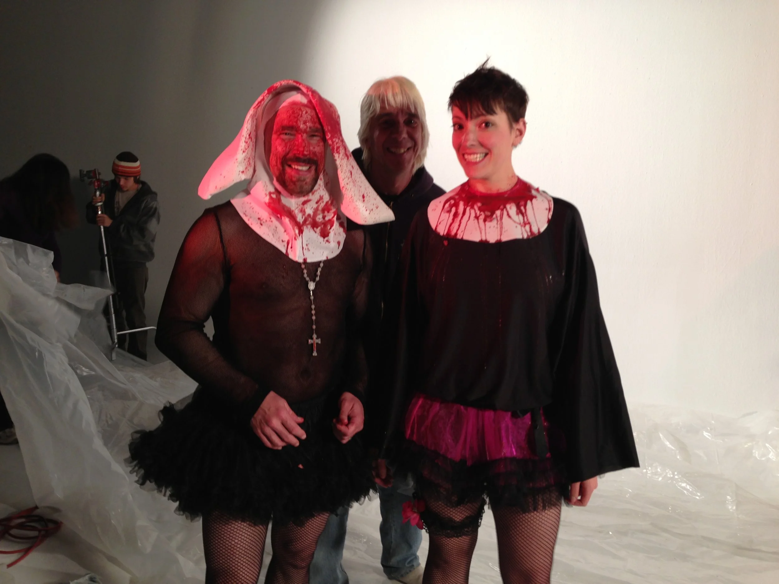 Vic Alejandro on the set of "Directors on Directing" dressed as a nun in a white habit and black tutu skirt standing in a studio with a female co-star with short black hair in a similar outfit and Director Damien with short bleached hair. 