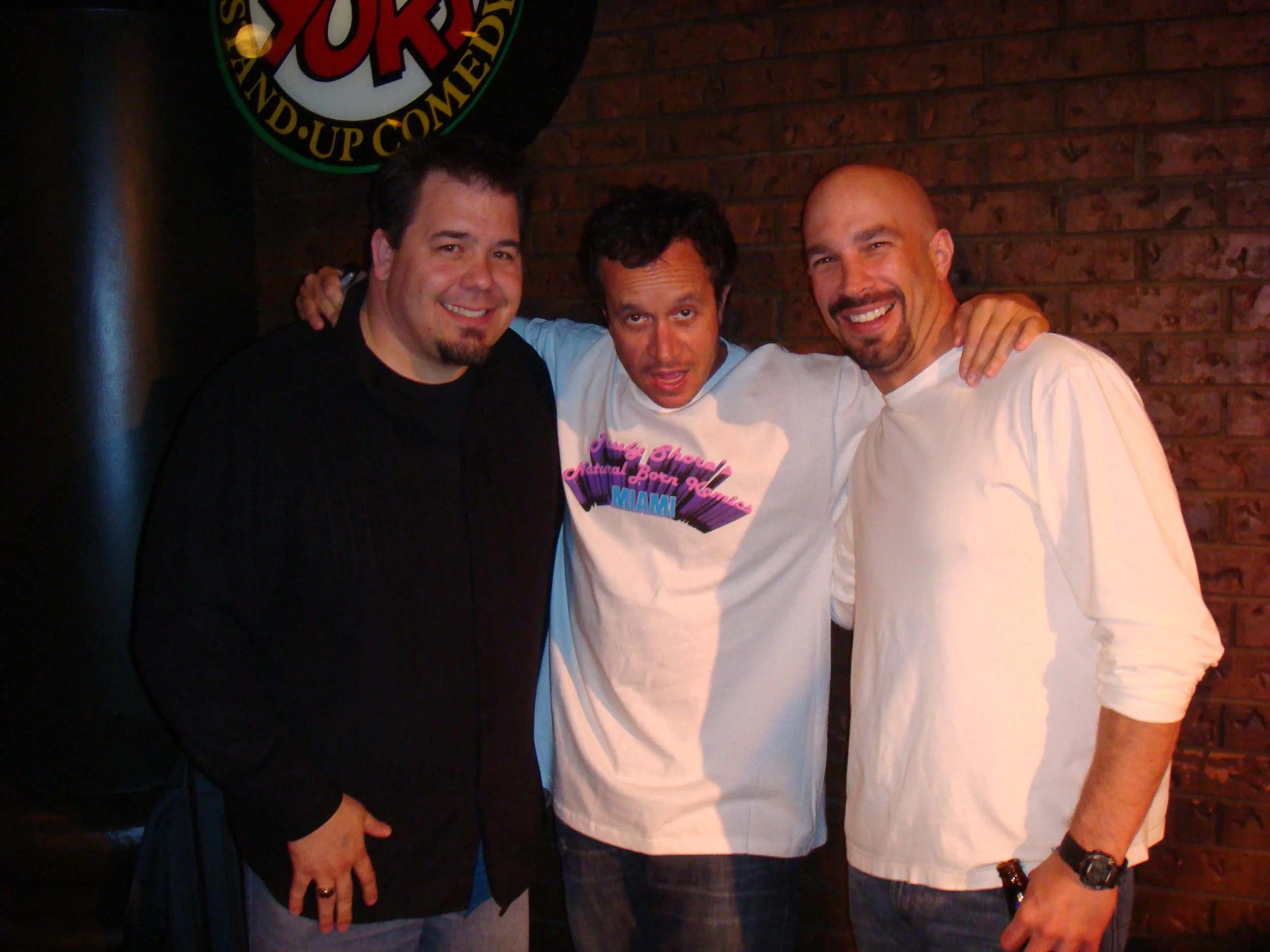 Vic Alejandro with comedians Pauly Shore and Jason Blanchard. Three men standing close together, smiling, with a brick wall background and a Yuk Yuks sign. This is from the Calgary Yuk Yuks.