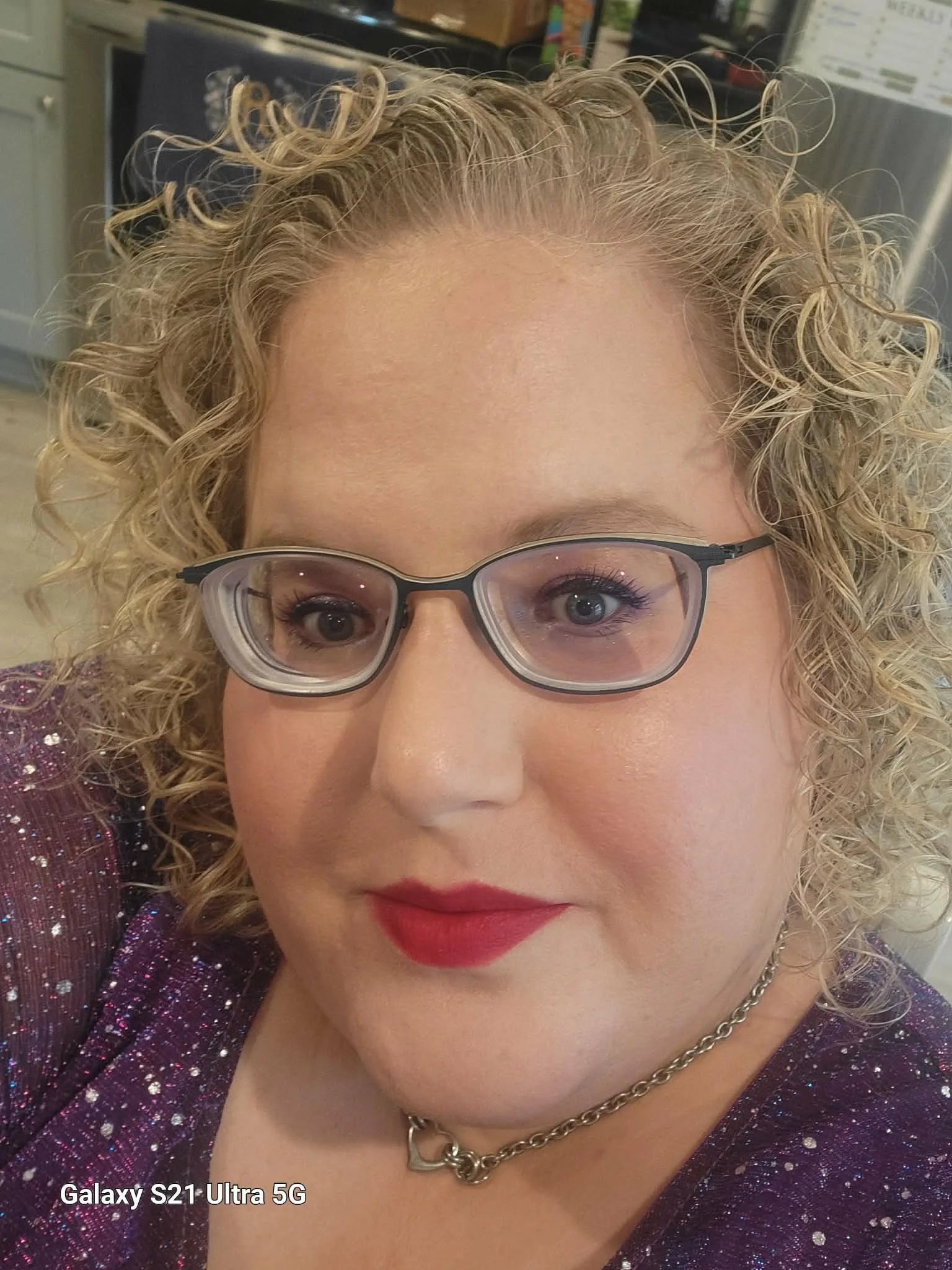 blonde curly haired white woman with red lipstick and blue glasses
