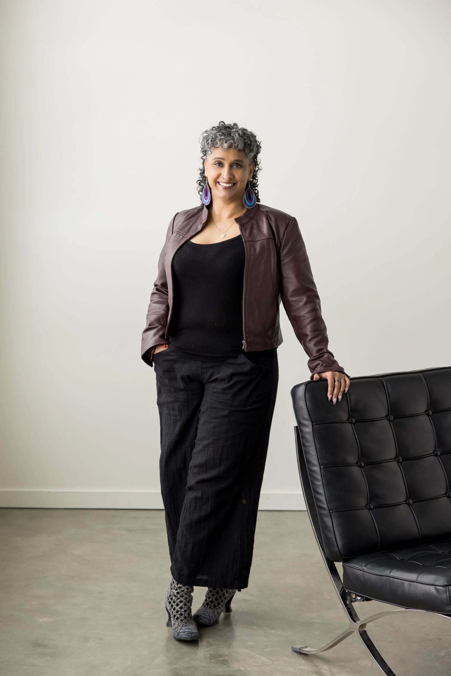 Woman standing beside a black office chair in an office or conference room with beige walls and a polished concrete floor.
