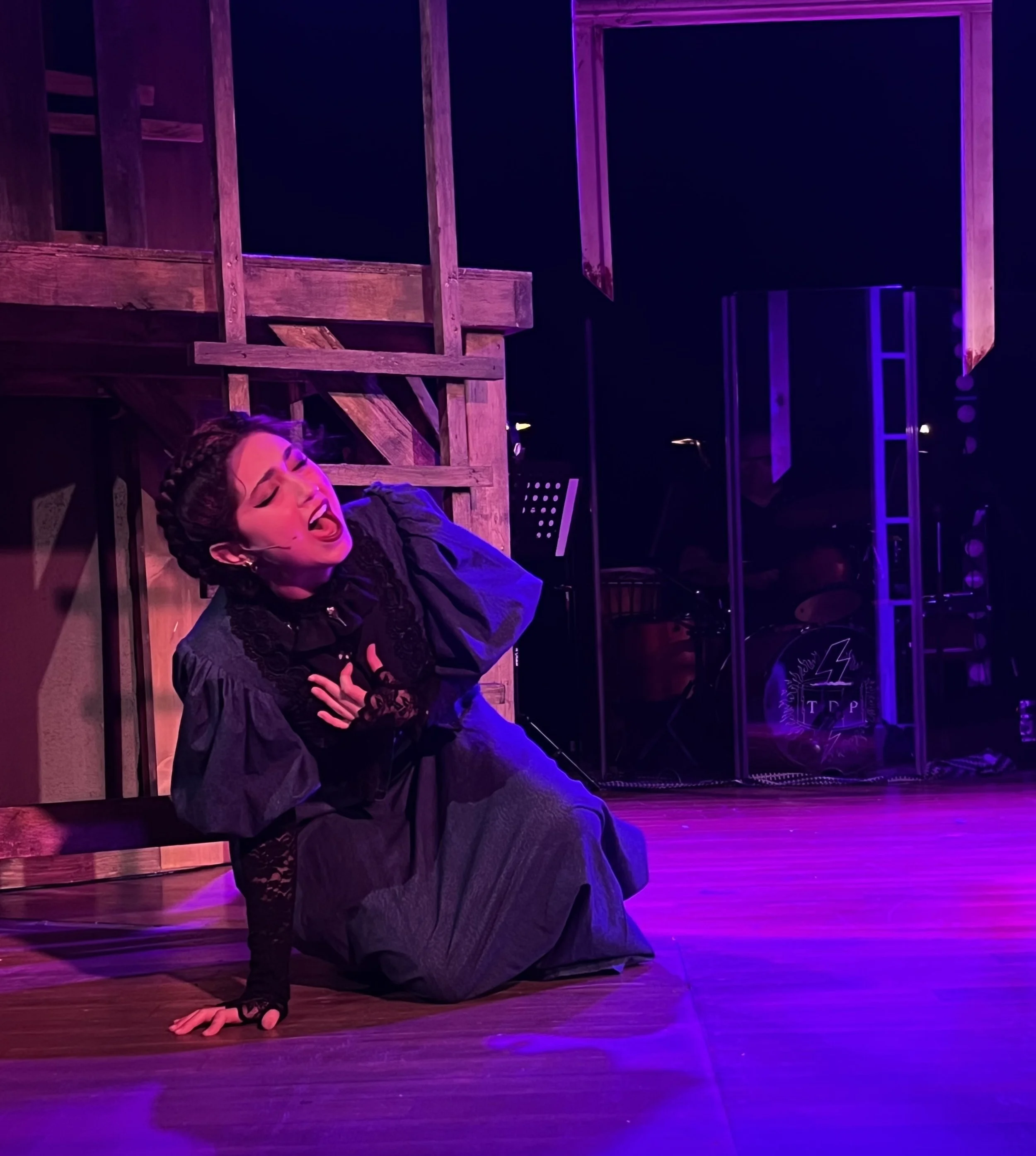 A performer in black clothing is doing a handstand on a stage with purple lighting, with a wooden structure behind them.