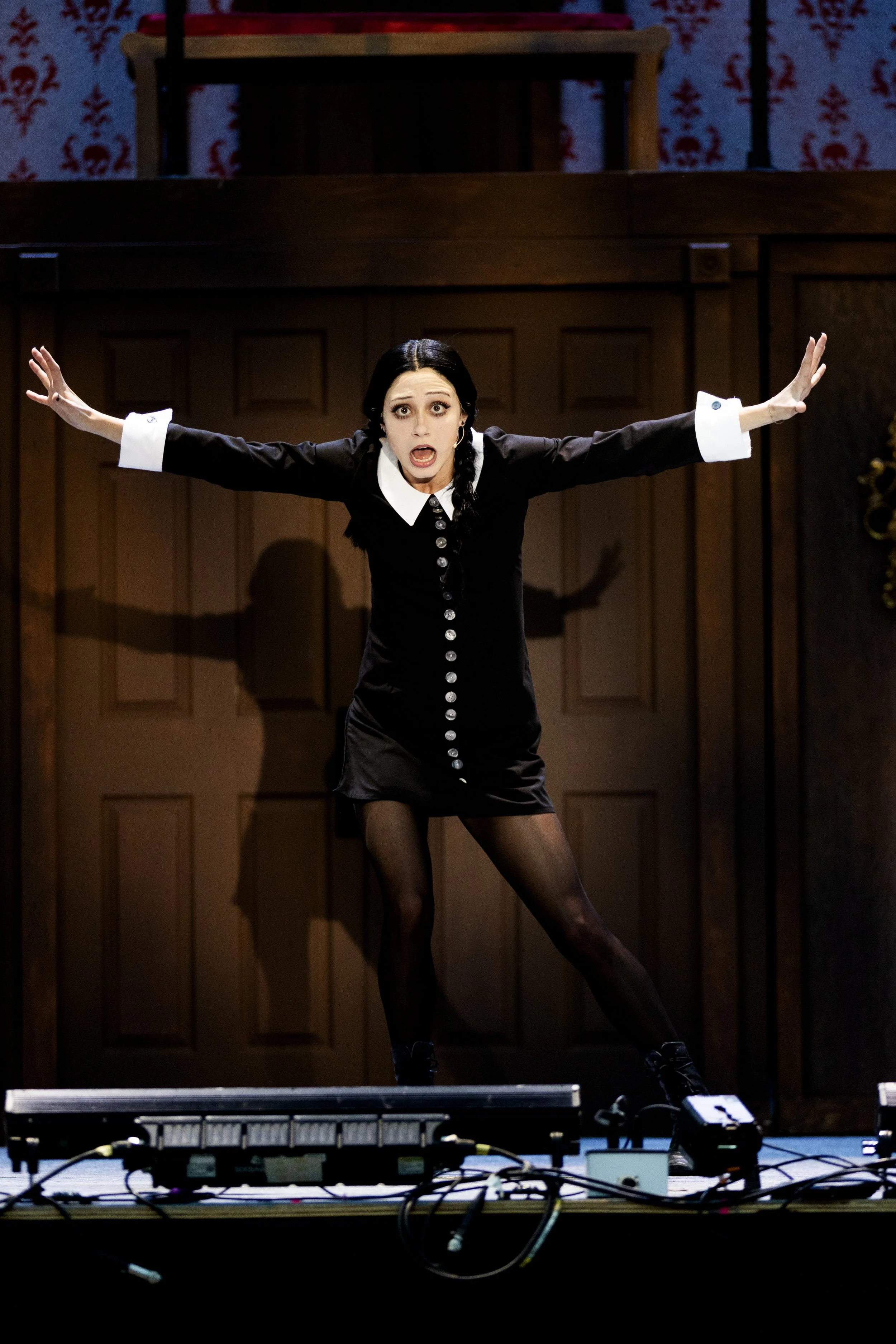 A woman dressed in a black and white outfit performing on stage with her arms extended, standing in front of a wooden backdrop.