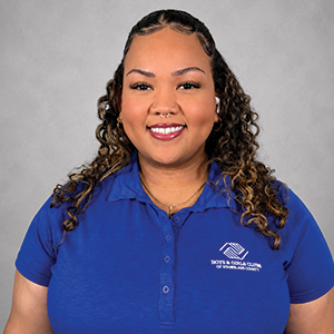 Portrait of a young woman with curly hair, smiling, wearing a blue polo shirt with a logo.